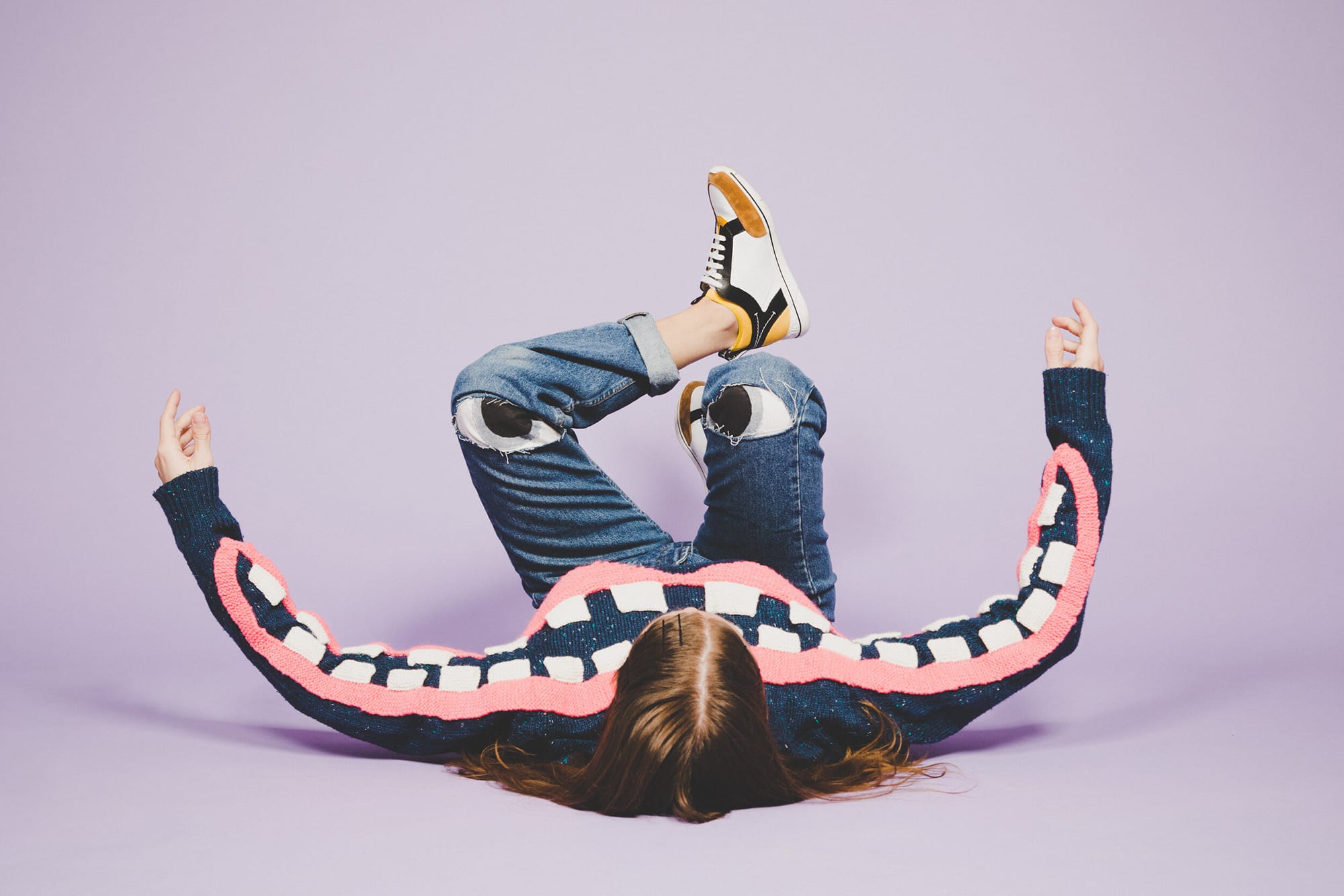 the artist on the floor wearing a sweater with a smile on the arms and eyes on her jeans