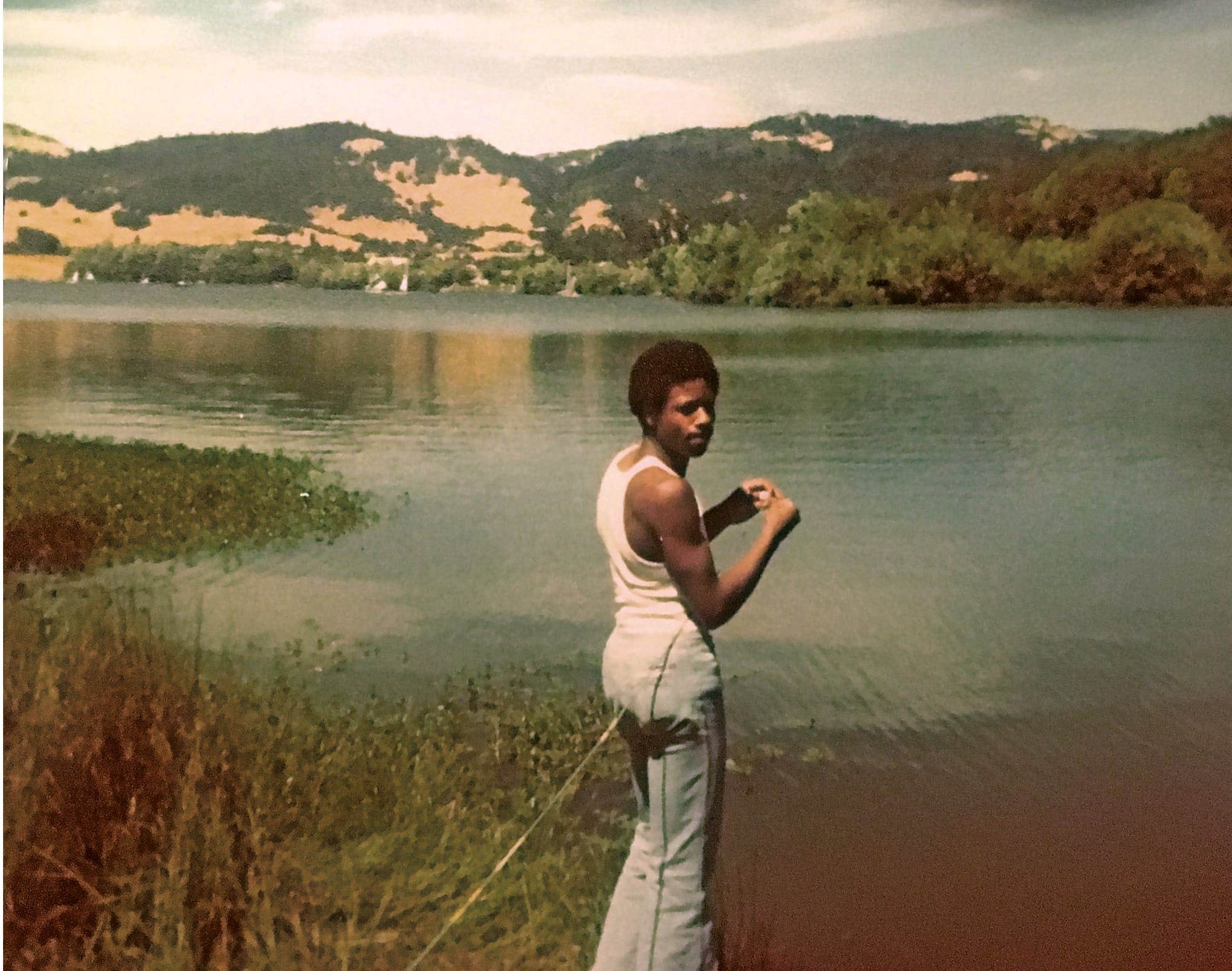 A man stands with a fishing pole in front of a lake