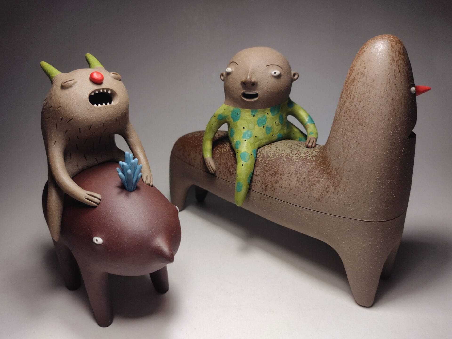 Two ceramic figures, each riding their own oblong-shaped snimal