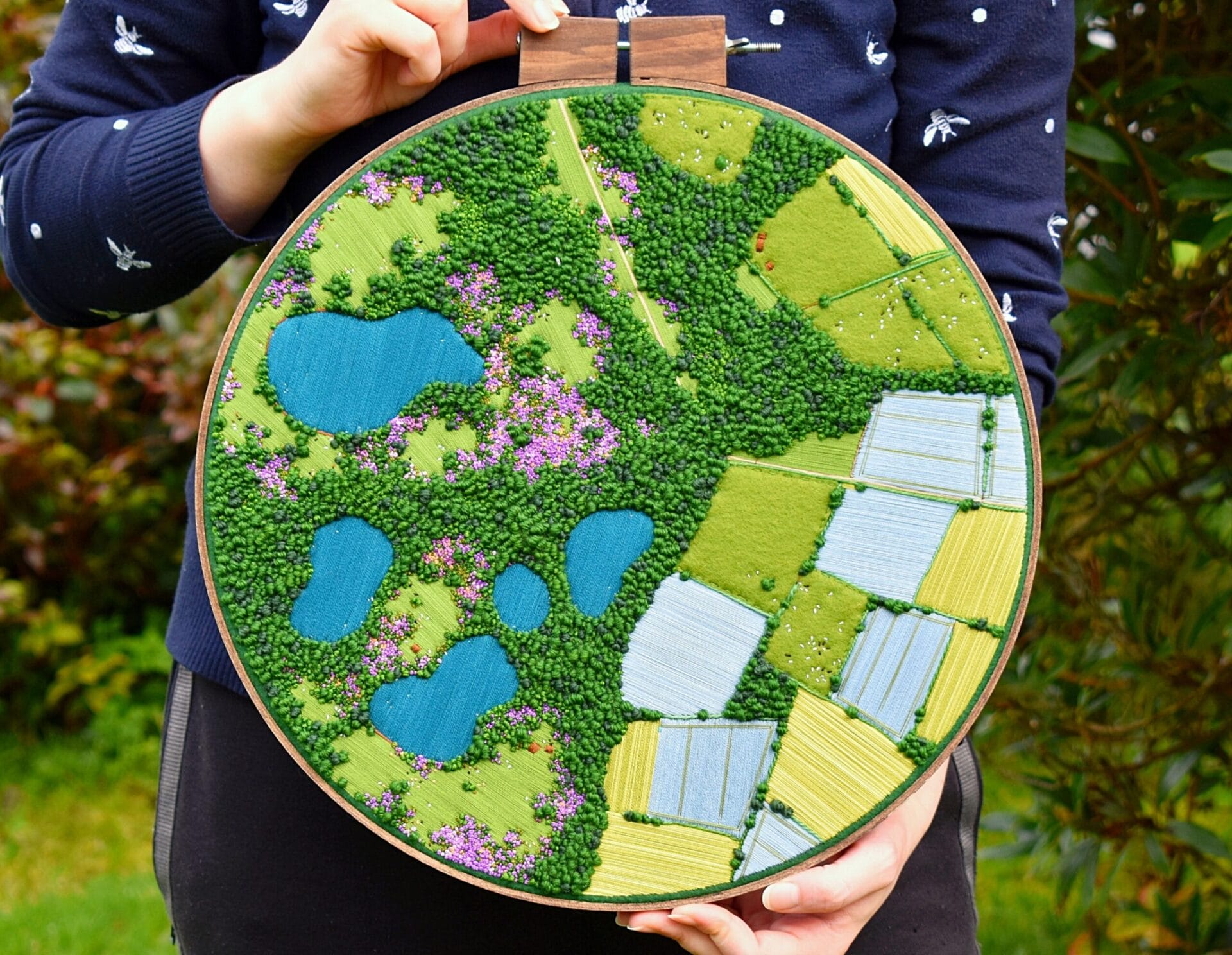 an aerial view of a green landscape embroidered inside of an embroidery hoop.