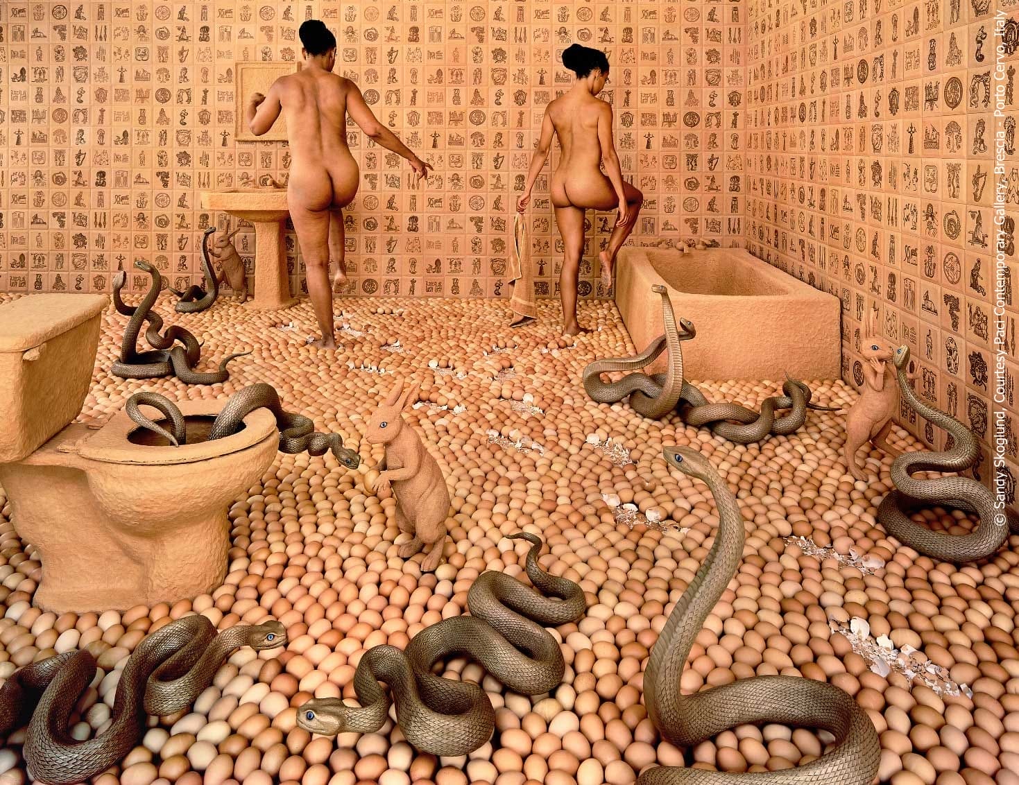 A fine art photograph of two women stepping over a bathroom floor covered in eggs. The floor also has numerous snakes and rabbits.