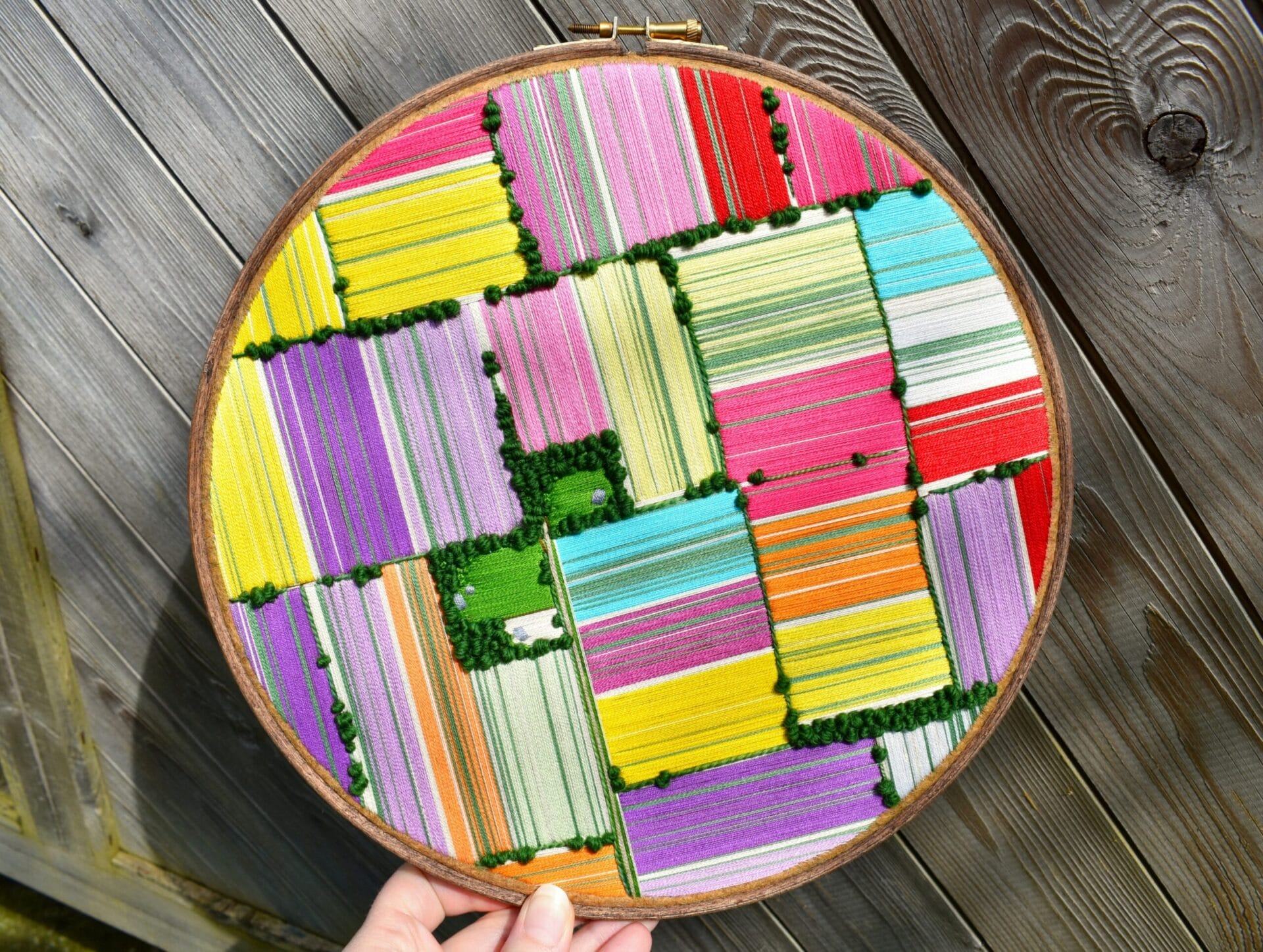 an aerial view of a colorful landscape embroidered inside of an embroidery hoop.