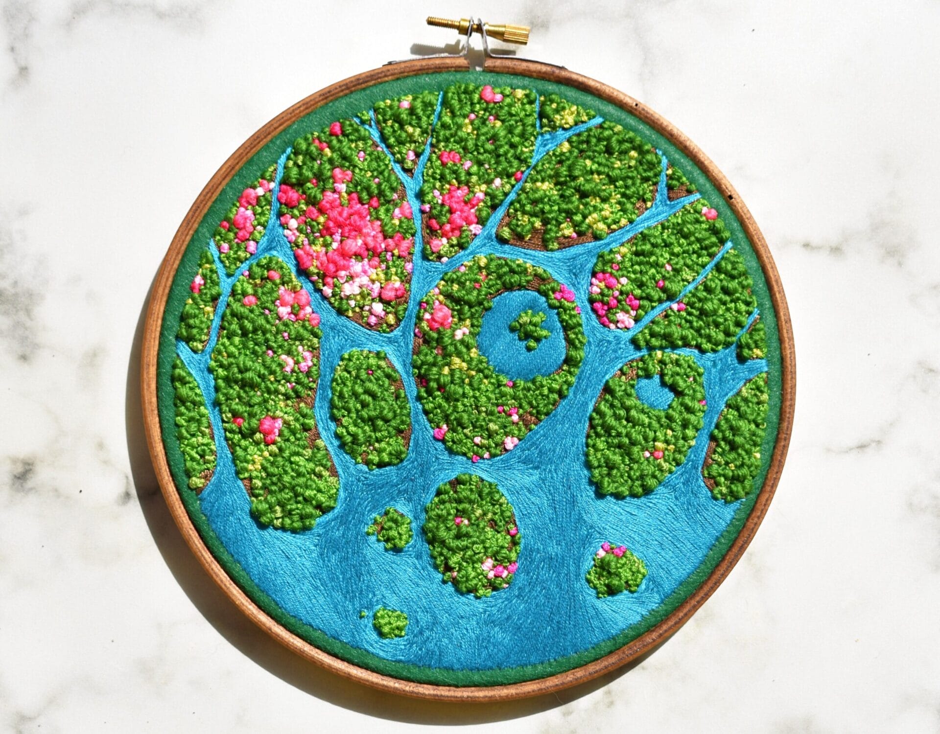 an aerial view of a green landscape surrounded by bodies of water embroidered inside of an embroidery hoop.