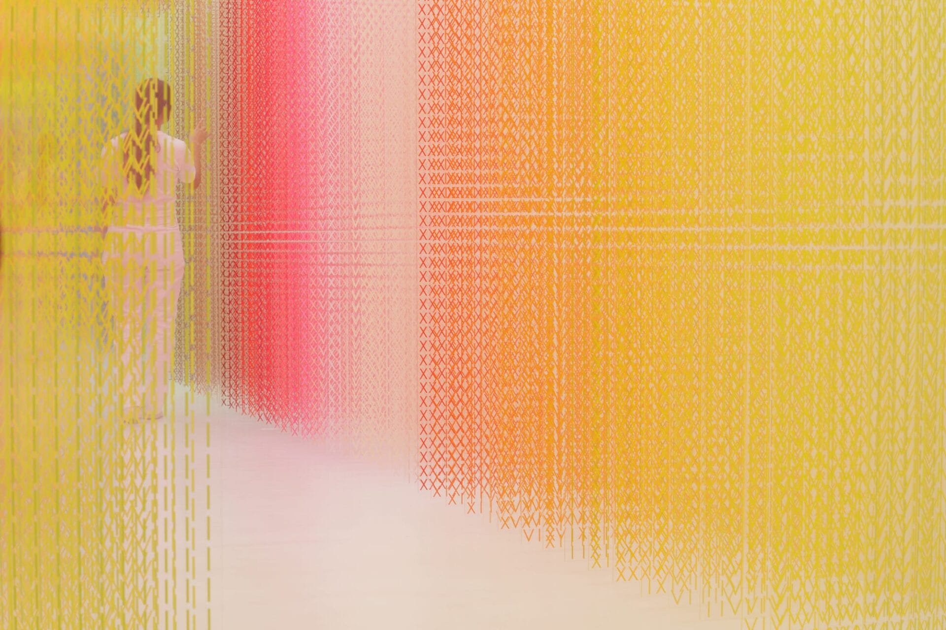 A figure walks through a large-scale installation made from thousands of brightly colored Roman numerals in a corridor that gradually changes color.