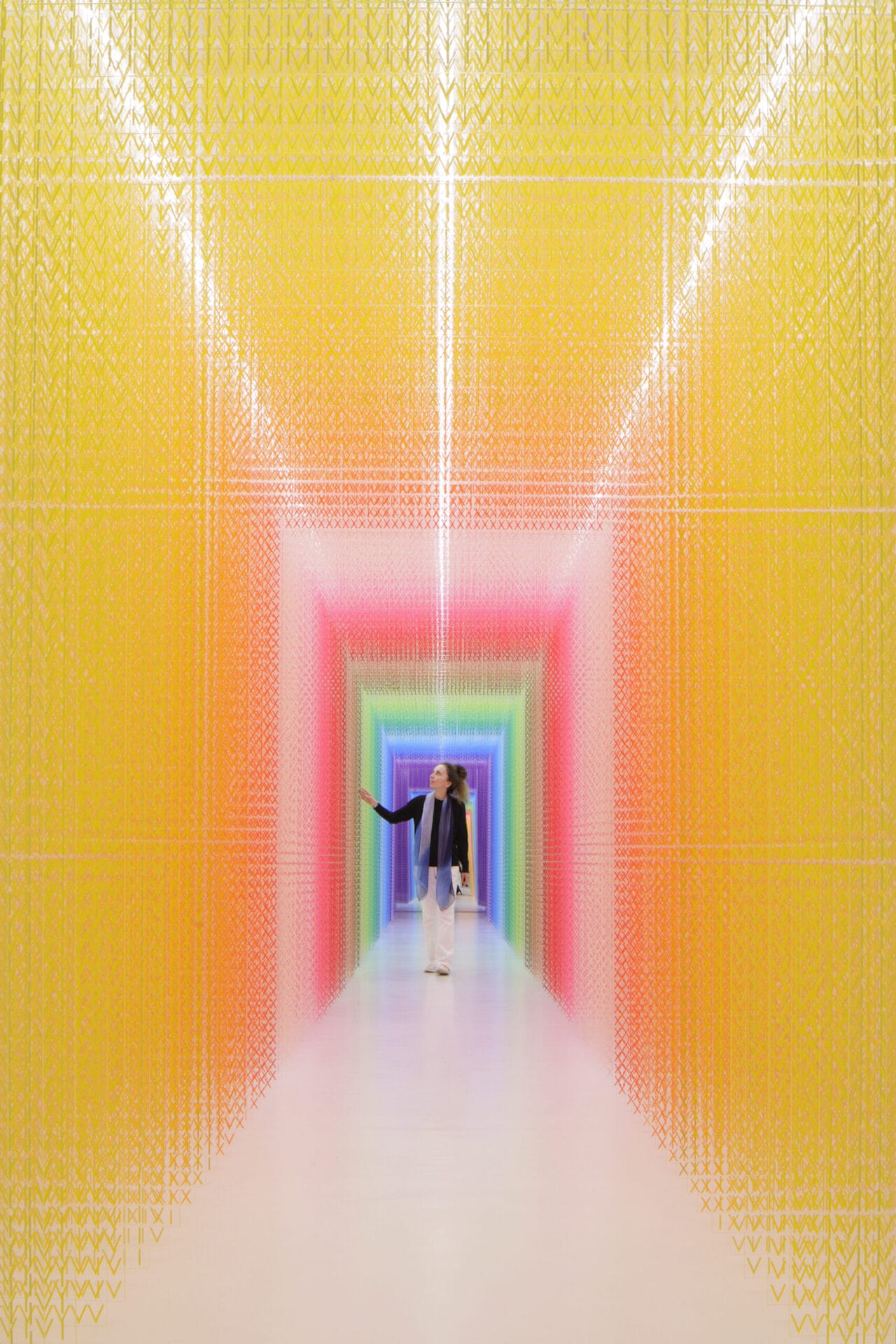 A figure walks through a large-scale installation made from thousands of brightly colored Roman numerals in a corridor that gradually changes color.l