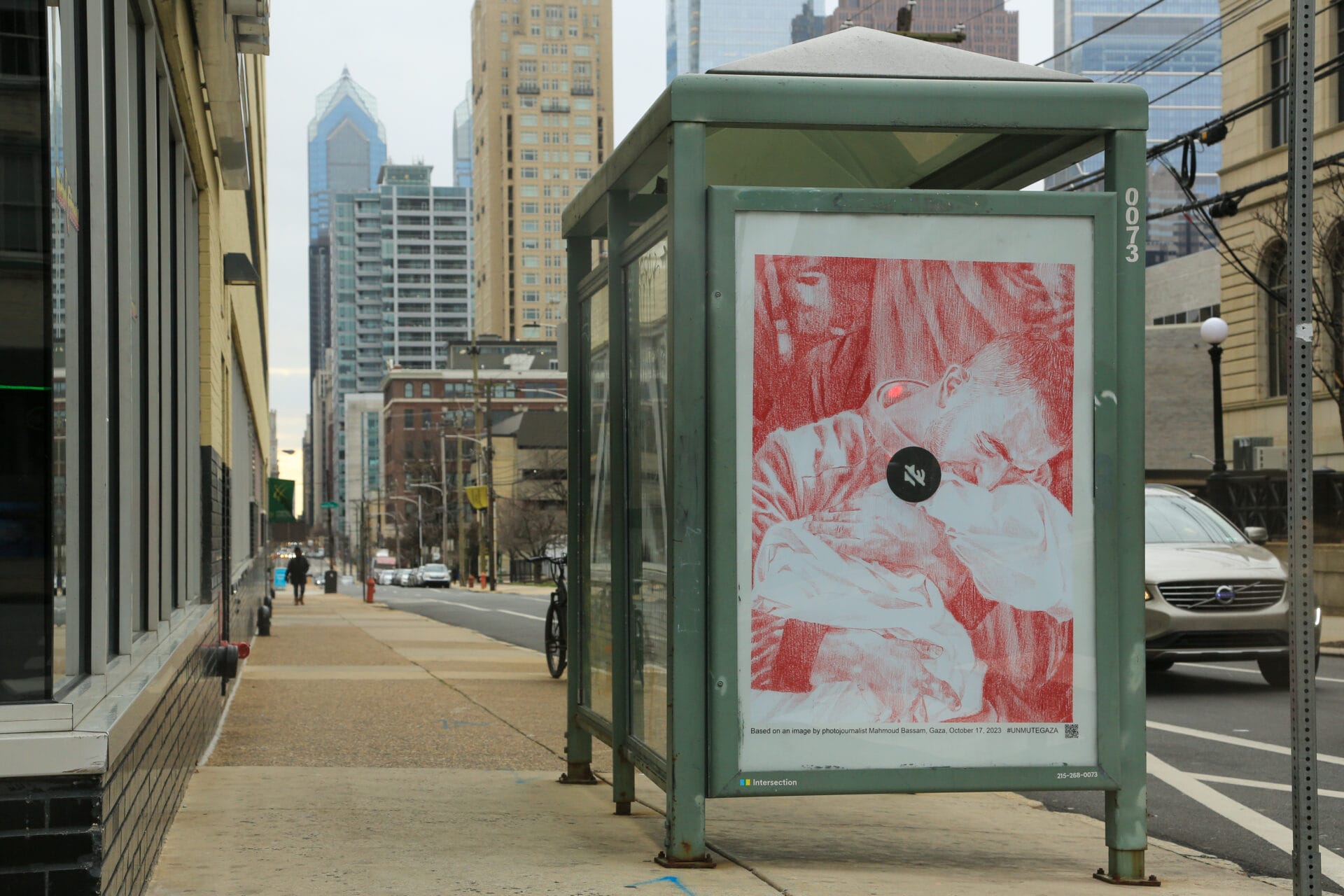 A poster is featured at a bus stop in a city. In the poster, a man clutches onto a baby he has lost, wrapped in white cloth.