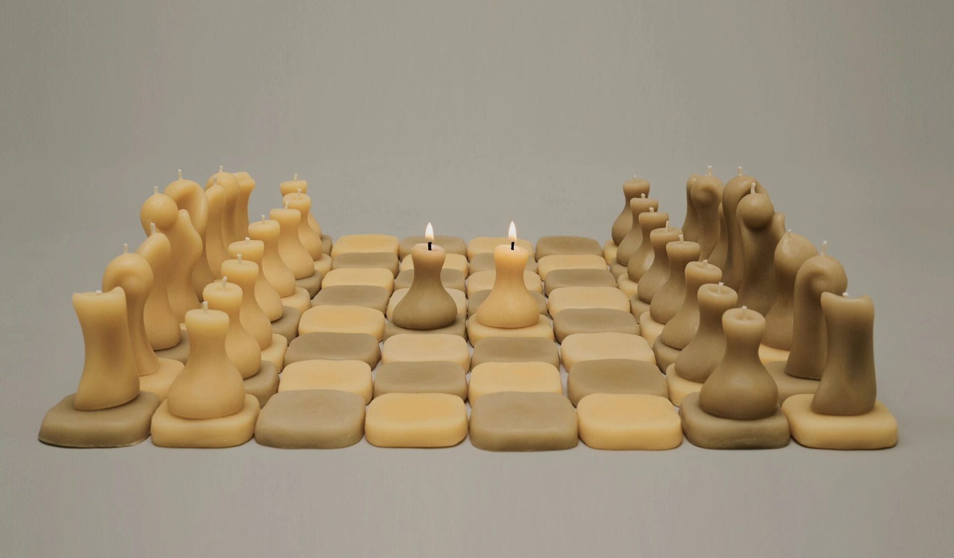 In hues of ivory and sage, 64 small squares made from beeswax come together together to form a checkered chess board. Minimalist chess pieces are placed on the board, in shades of ivory and sage with wicks, as each is a candle.