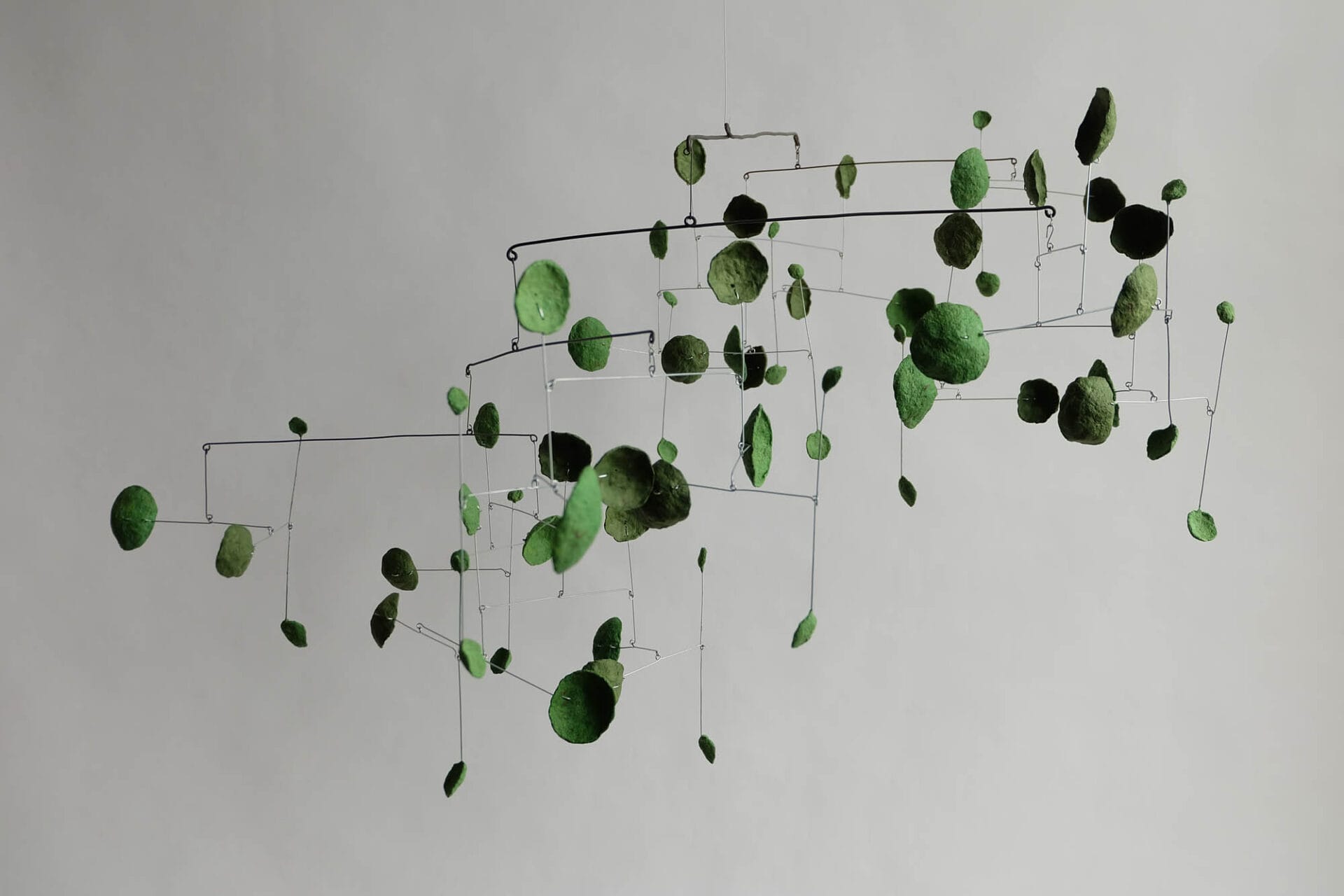 A mobile is suspended in the sky, made from wire and pod-like paper pulp shapes in shades of green.