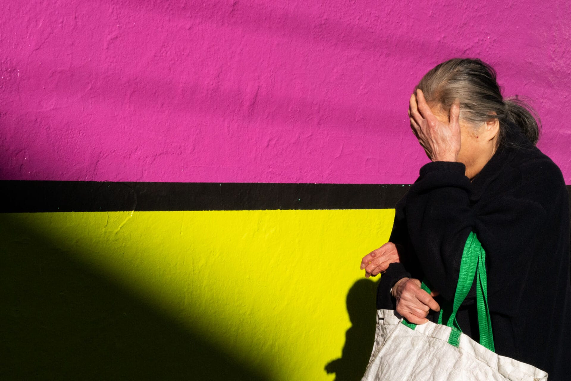 Against a magenta and yellow background, a woman shields her eyes from the sun.