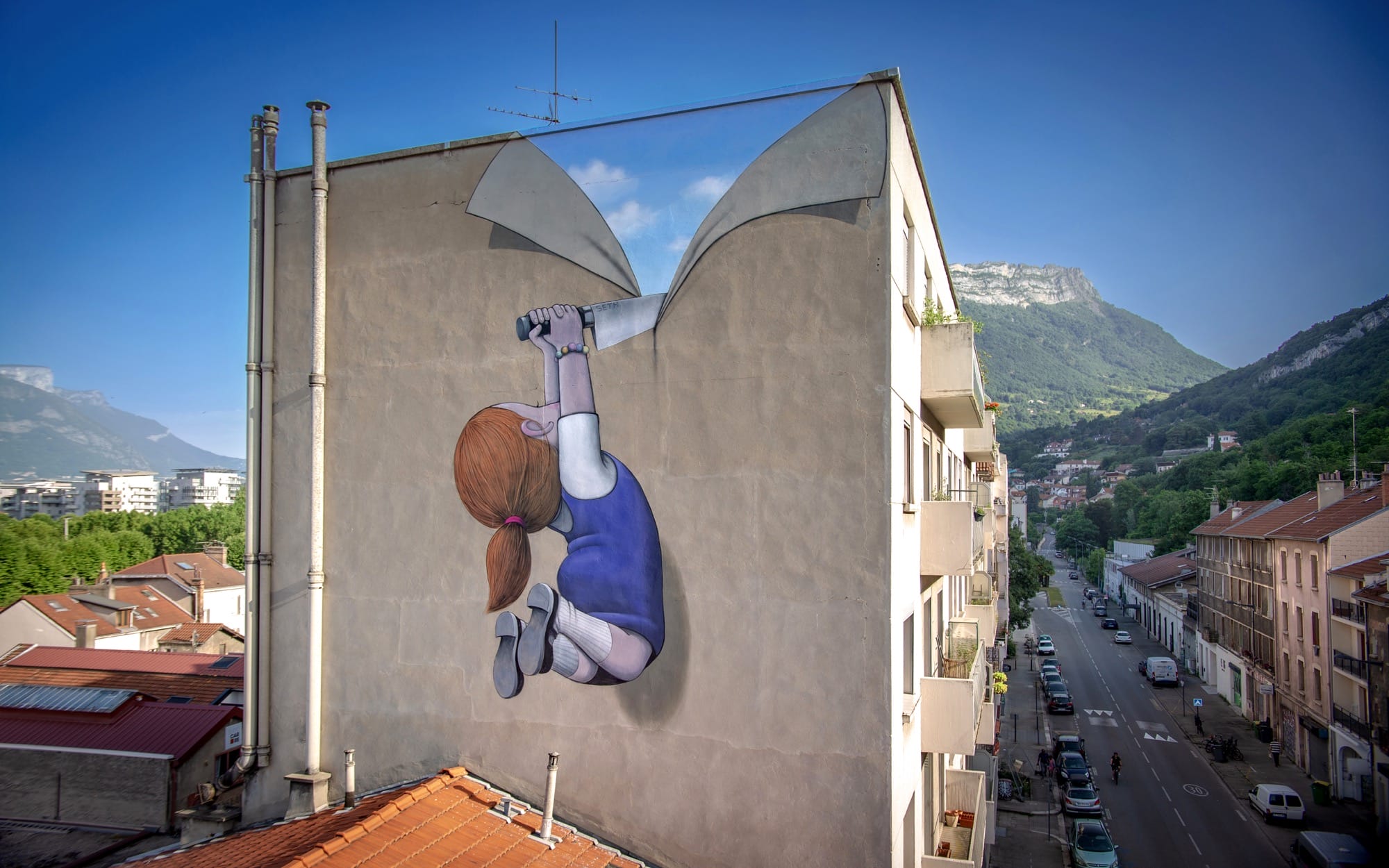 a mural on the side of an apartment building in Grenoble, France, of a young girl slicing open the wall with a large knife and revealing a bright blue sky inside