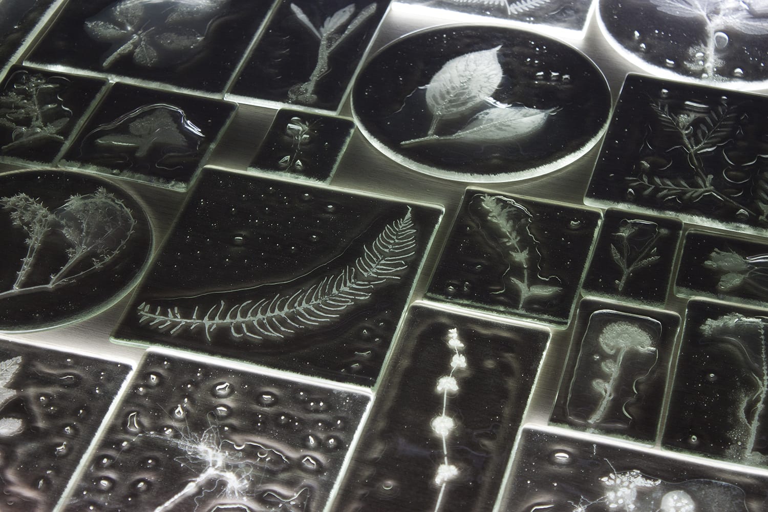 a detail of a multi-paned glass wall sculpture featuring a clear rectangle of solid glass with a frosty impression inside of plants with bubbles