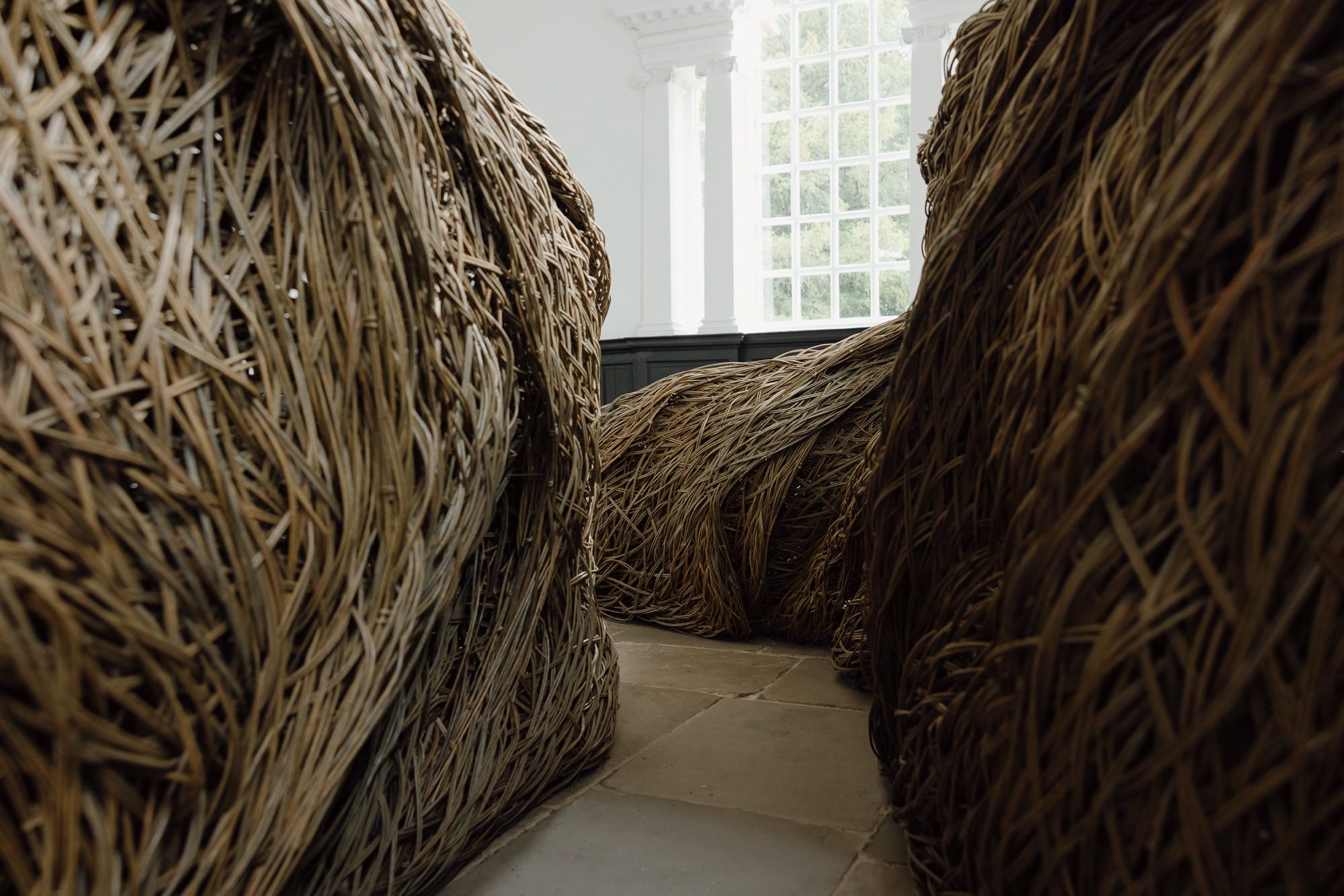 a detail of a sculptural installation that moves through an architectural space, made of woven willow branches