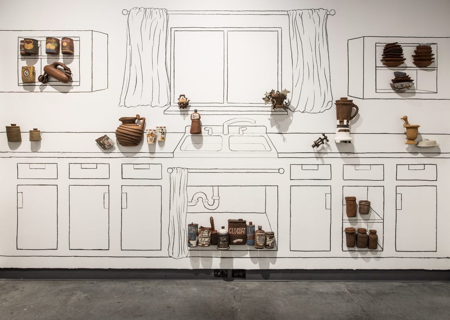 a gallery wall outlined with kitchen cabinets and counters, with three-dimensional reliefs of ceramic vessels and objects installed on the wall