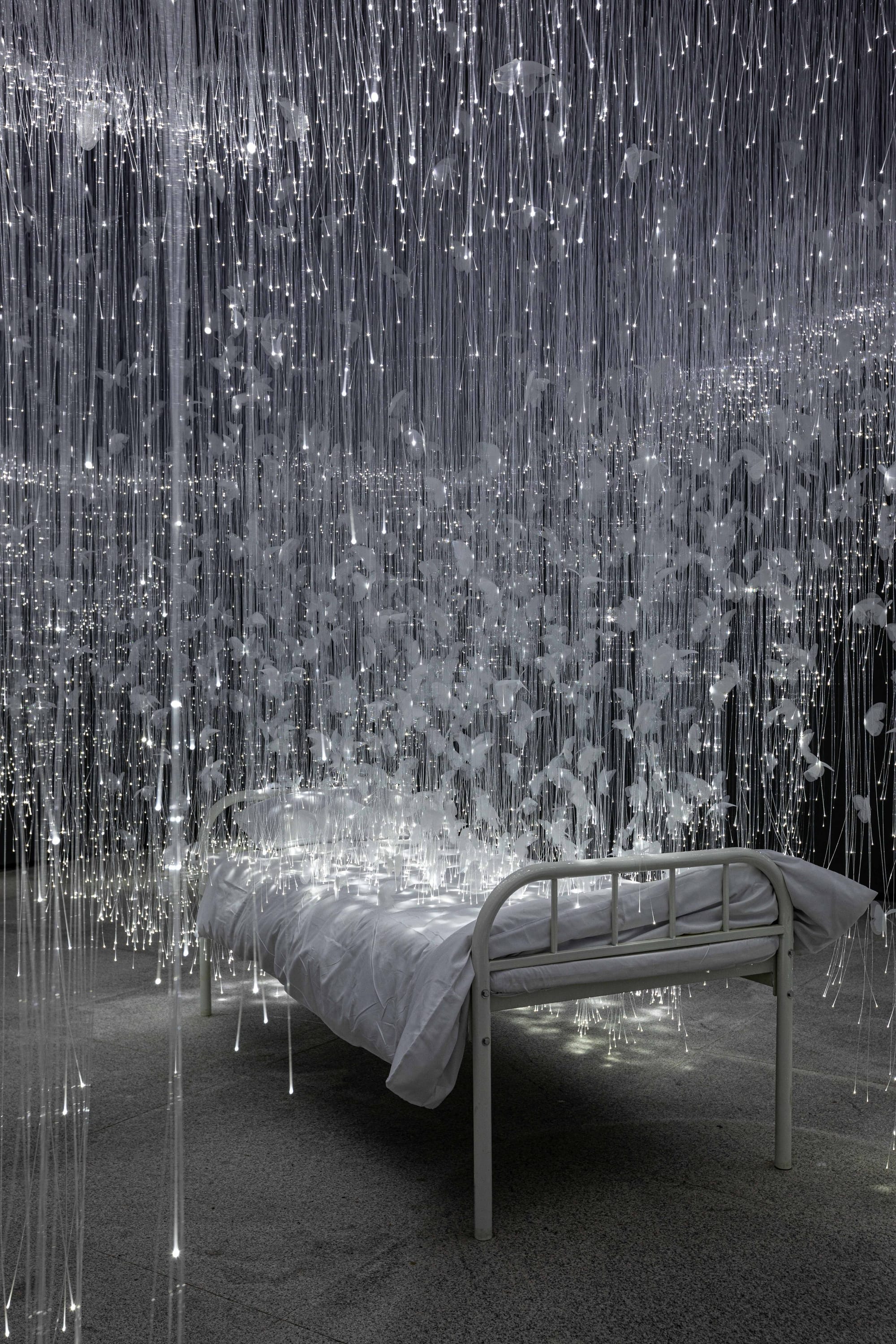 white glimmering tendrils dangle around a small twin bed