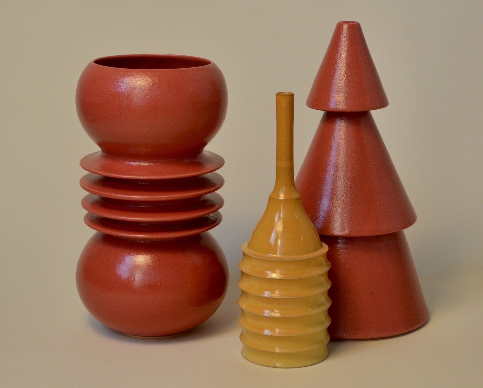 three geometric vessels in bright red and deep yellow