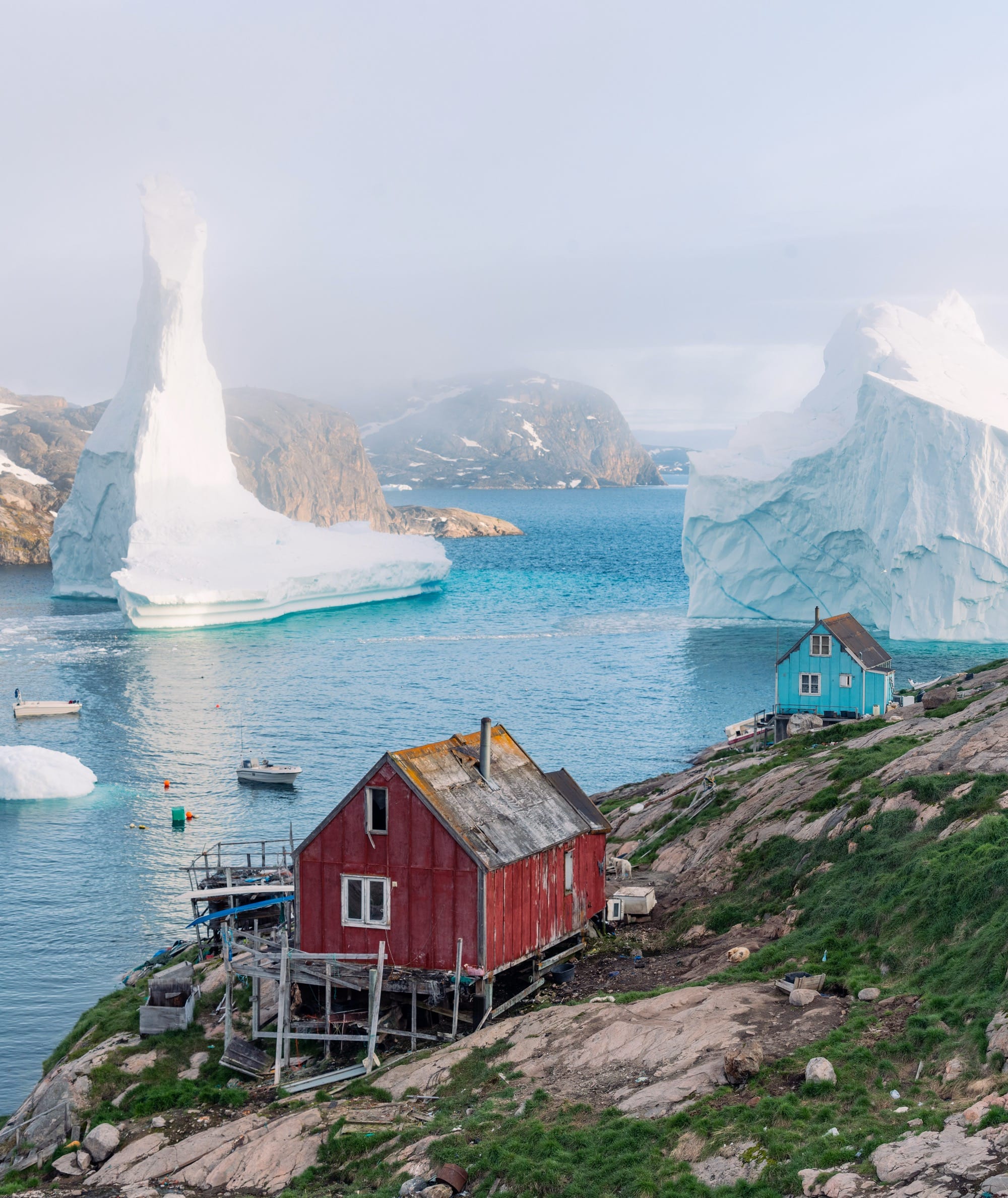 a small house in Greenland with two giant icebergs in the background