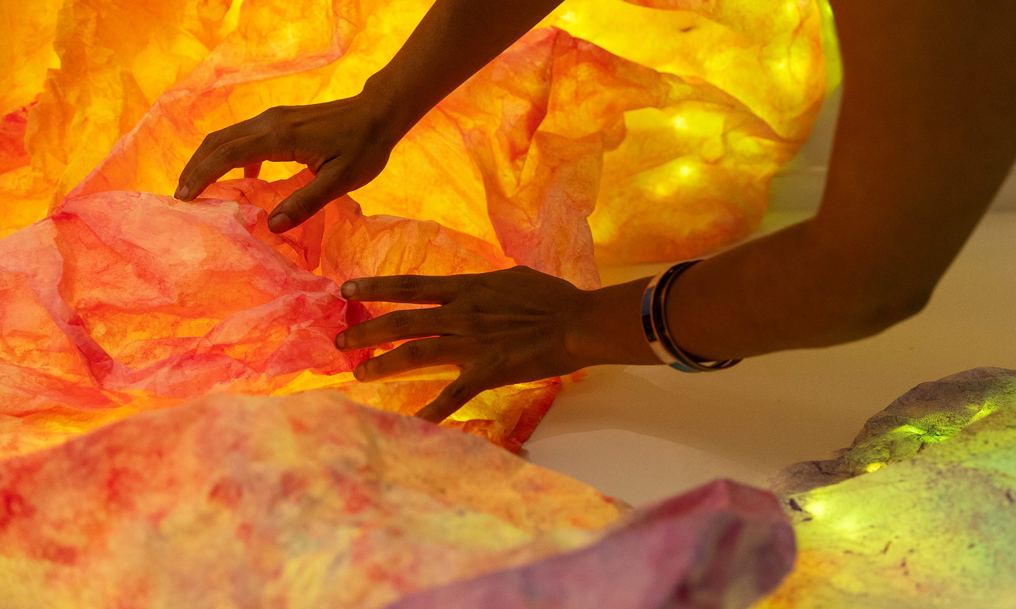 two hands reaching out to mottled fabrics in oranges and yellows