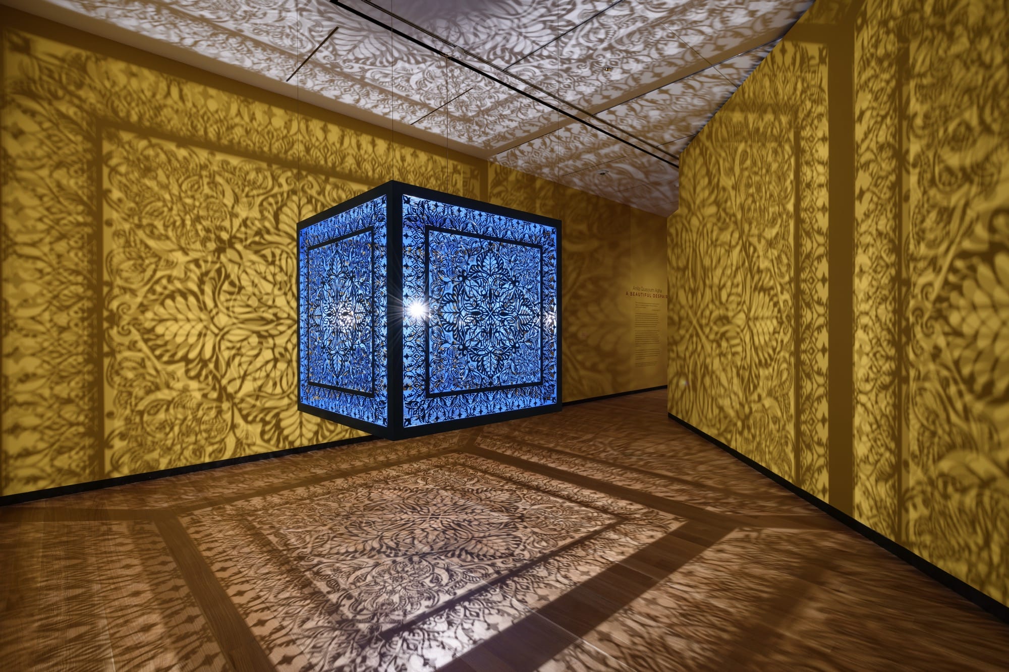 a sculptural installation in a yellow room, with light emitting from within a structure that casts ornate shadows onto the walls