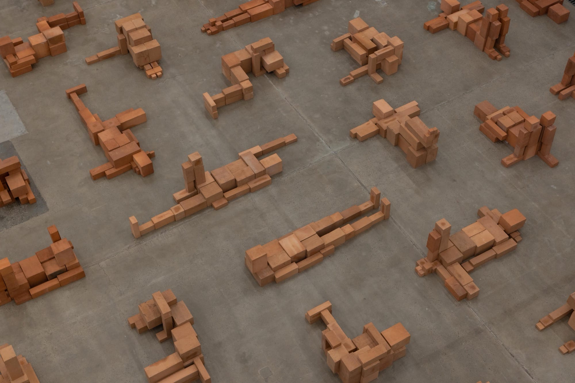 a detail of a room-size art installation by Antony Gormley of blocky terracotta forms resembling human figures in various positions