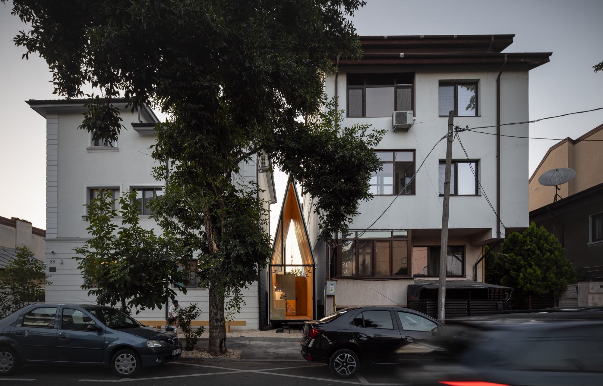 a tiny, contemporary cafe with a steep, pointed roof sits between two larger conventional buildings, designed by Vinklu