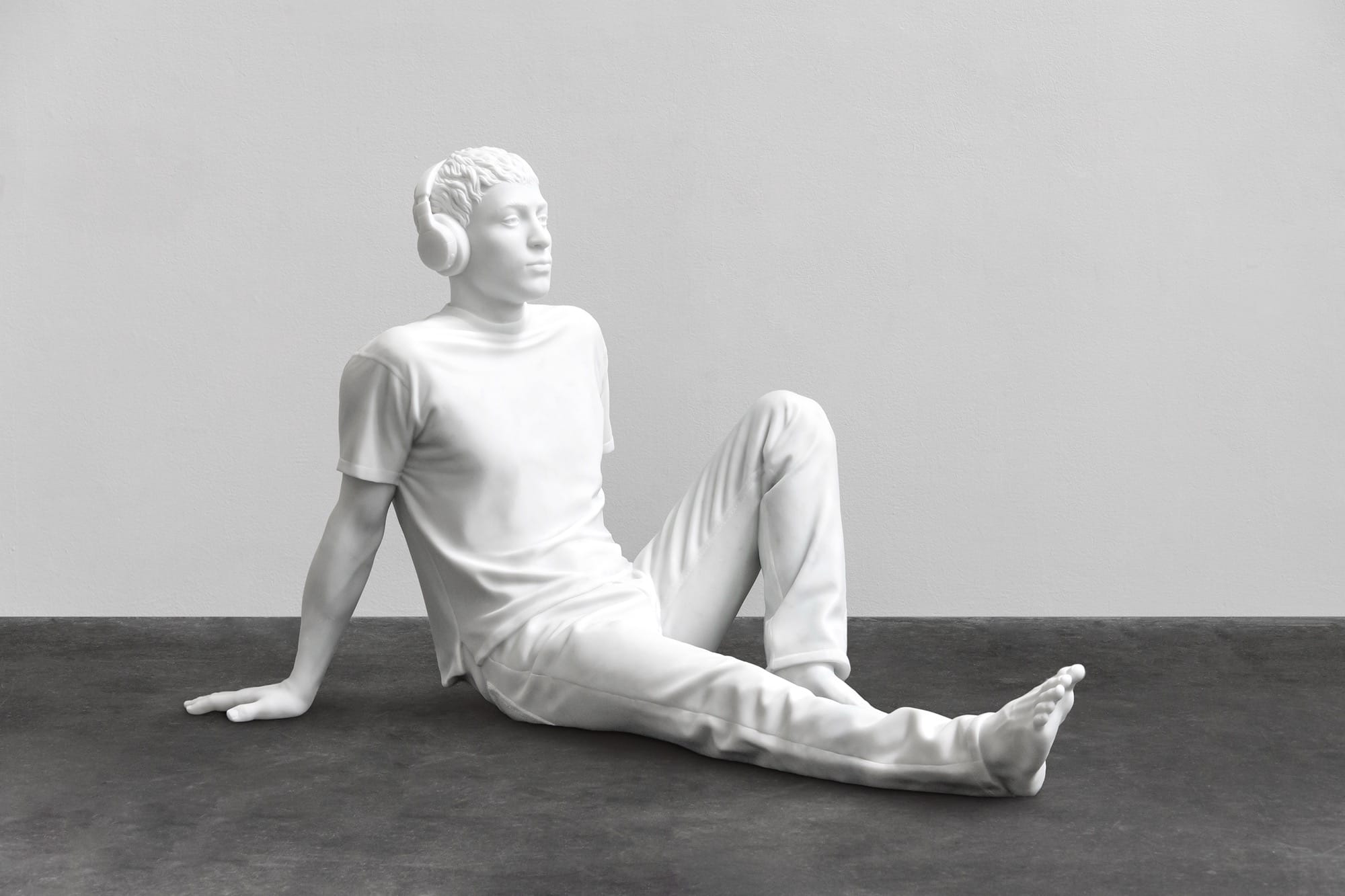 a sculpture by Elmgreen and Dragset of a white figure resting on the floor wearing headphones