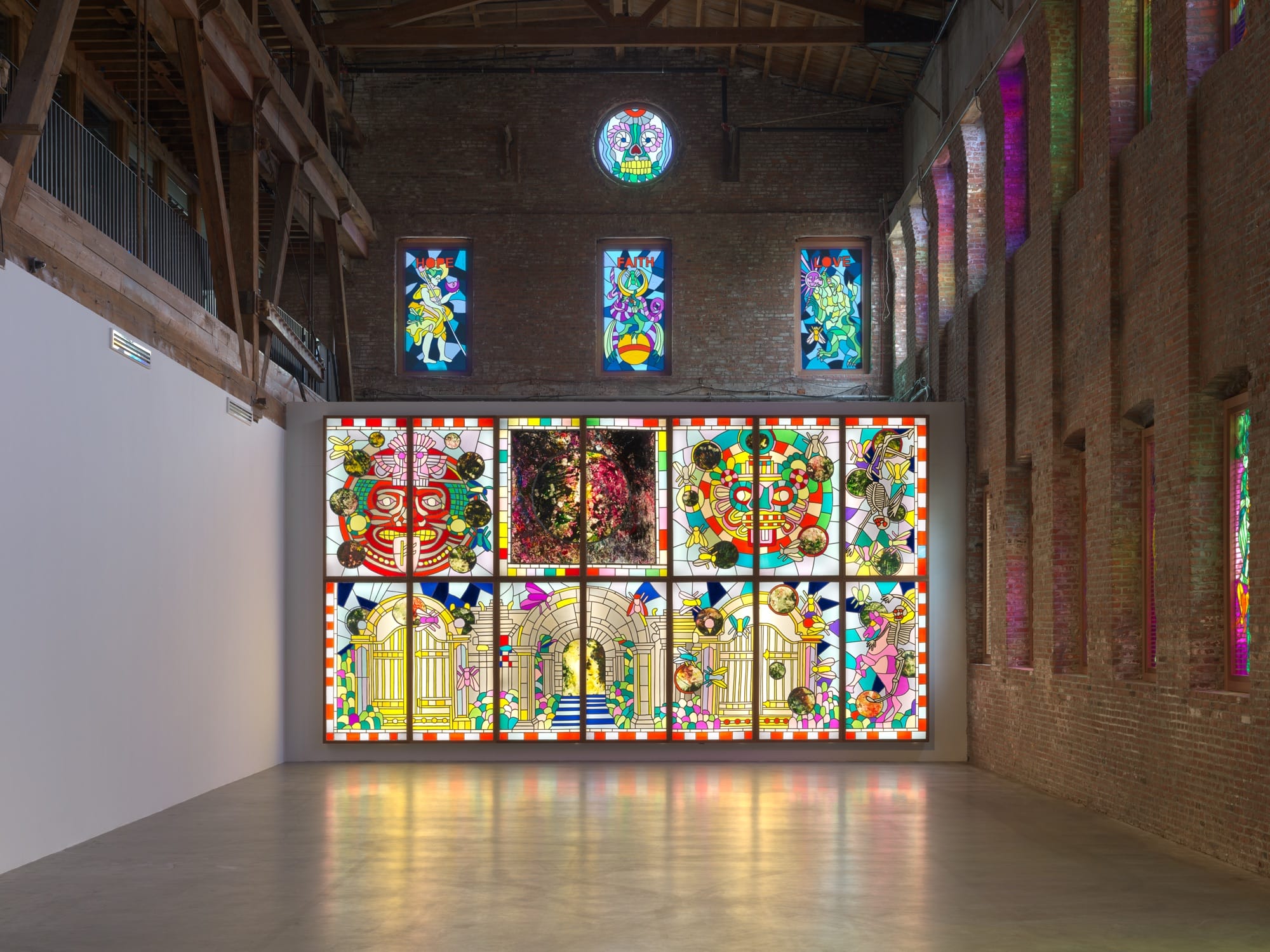 an installation by Raul de Nieves of a colorful lightbox mural with deities and skeletons along with smaller window fitted pieces