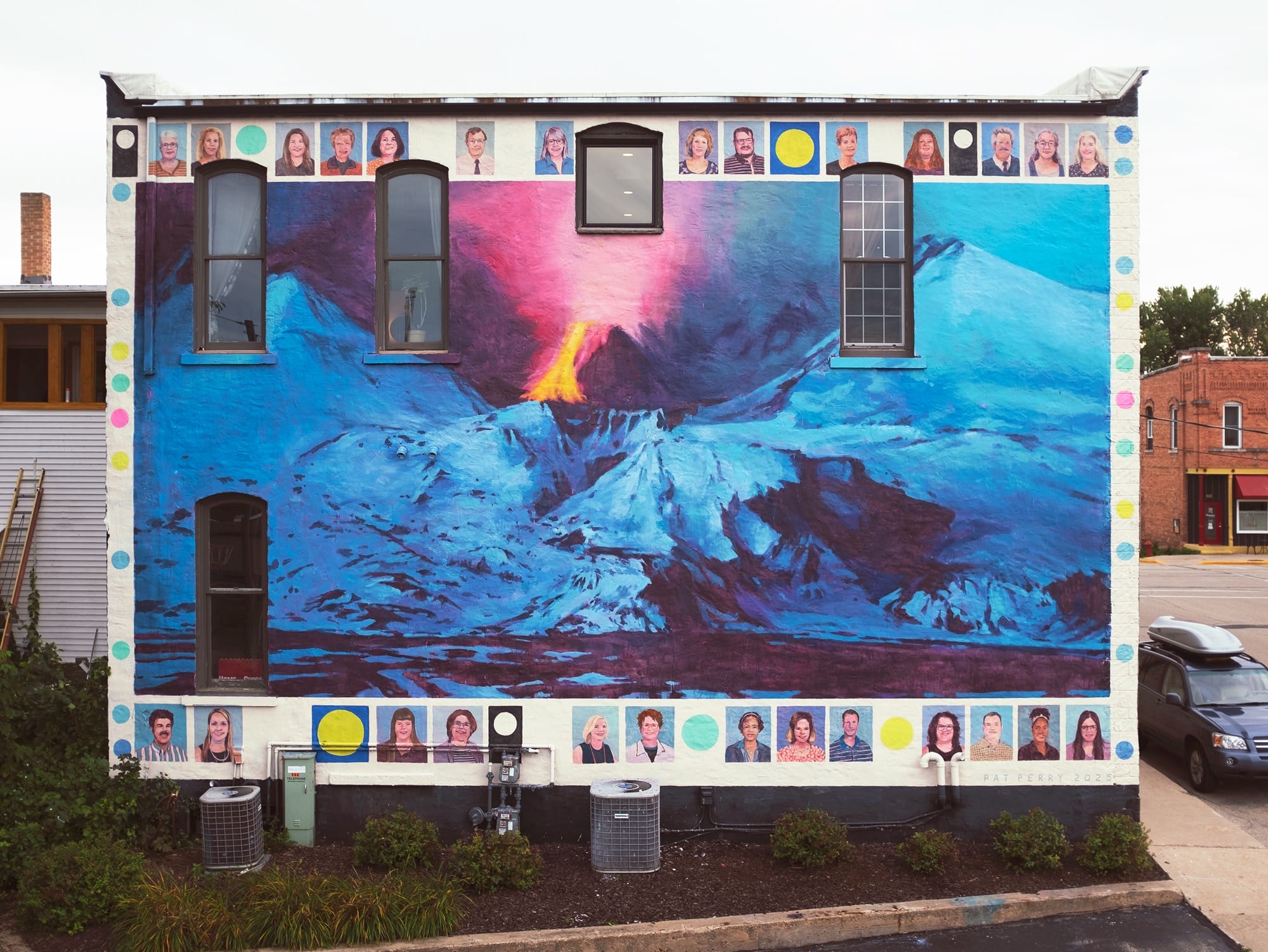 a mural by Pat Perry of an exploding volcano and snow-covered mountains. a top and bottom border features portraits of schoolteachers