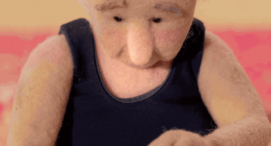 a gif from the short animated film "Madeleine" by Raquel Sancinetti, featuring a stop-motion puppet of an old woman pointing a camera toward her own face, which then cuts to a real video of an elderly woman's eyes