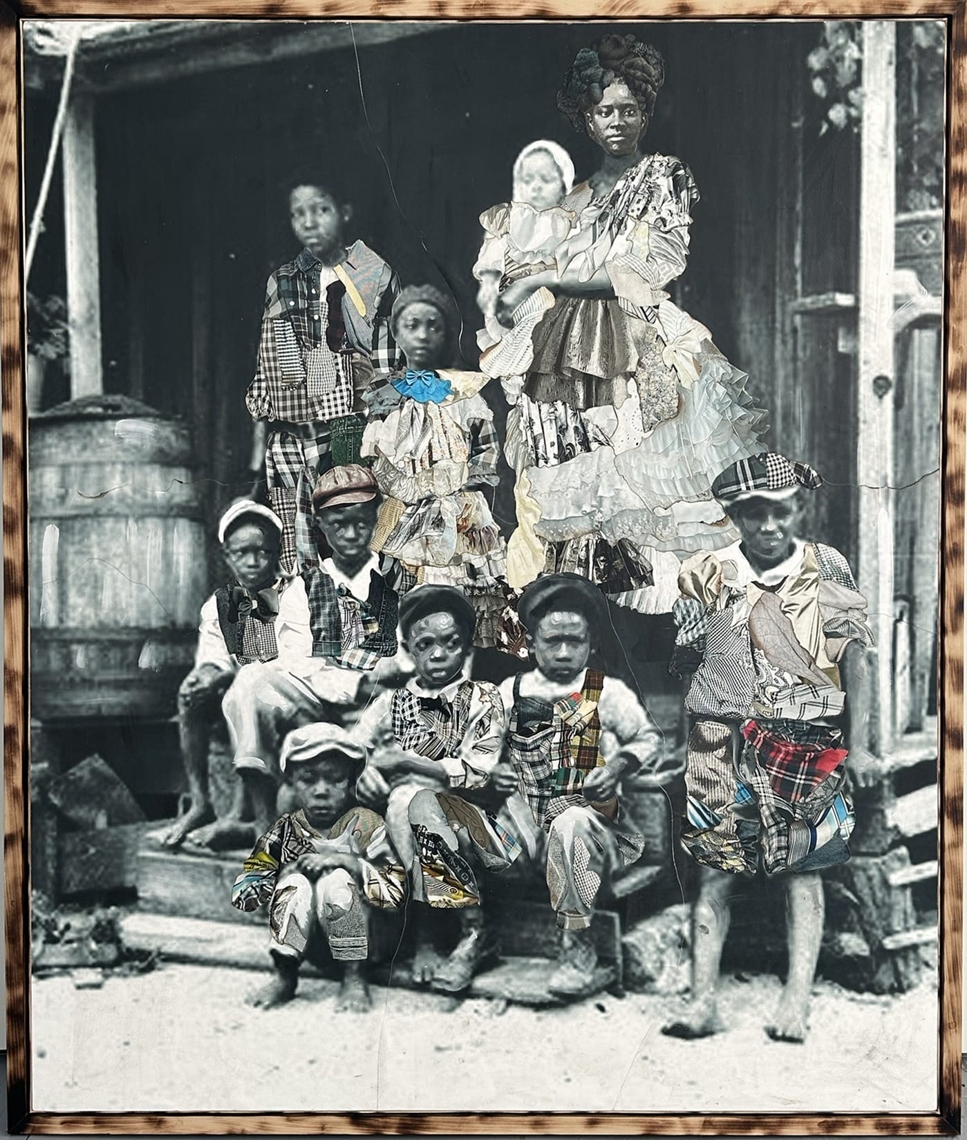 a framed portrait by Stan Squirewell, from an old photograph, of a large group or family seated on the porch a house, with colorful, patterned fabrics painted onto the image