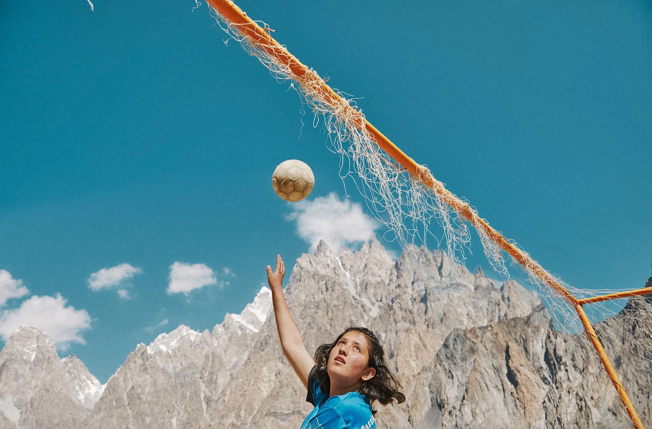 a Pakistani girl playing soccer with the mountains in the background