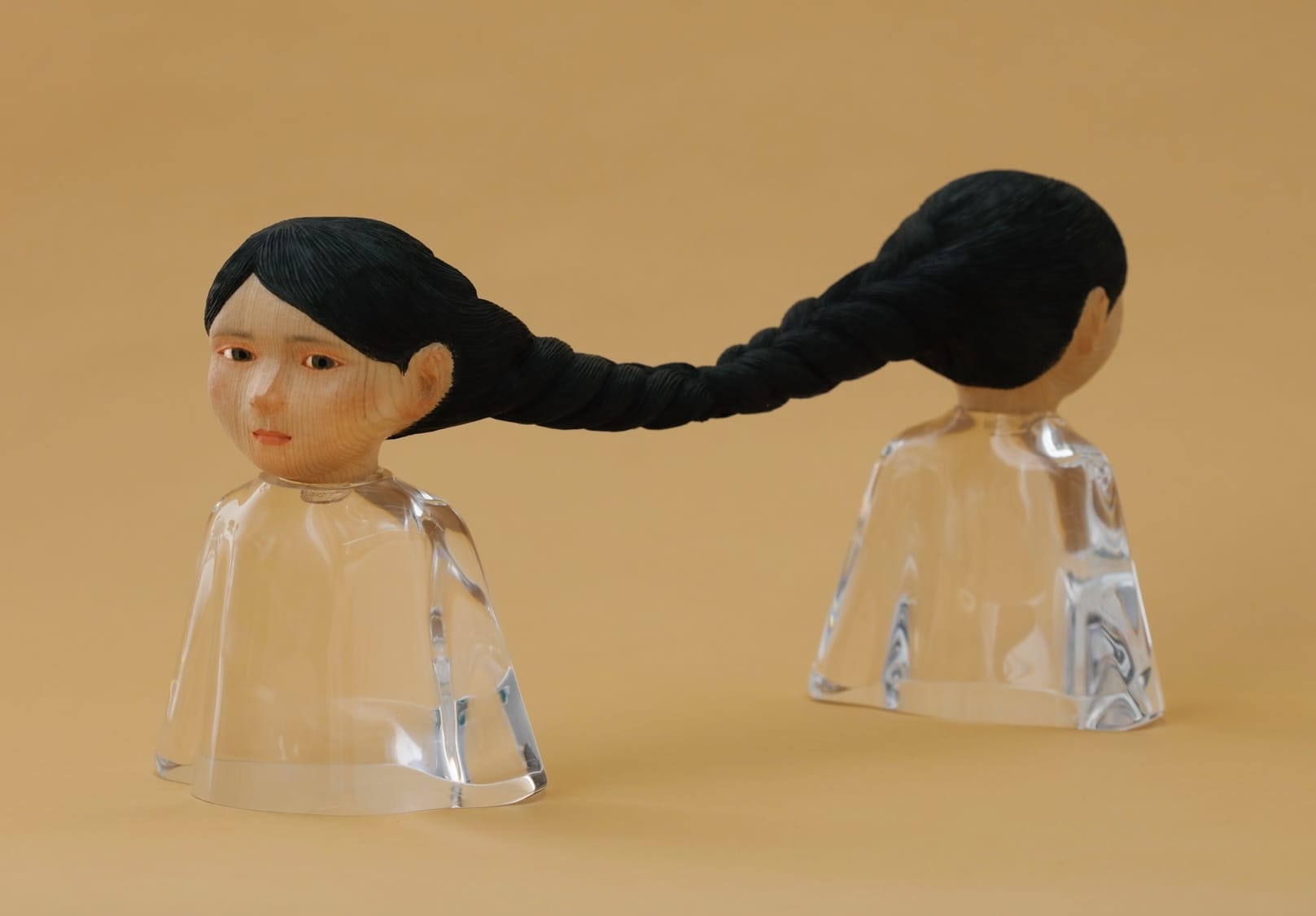 a small sculpture by Ayako Kita made of cypress and acrylic resin, depicting two female figures standing back-to-back with long black hair that is braided together