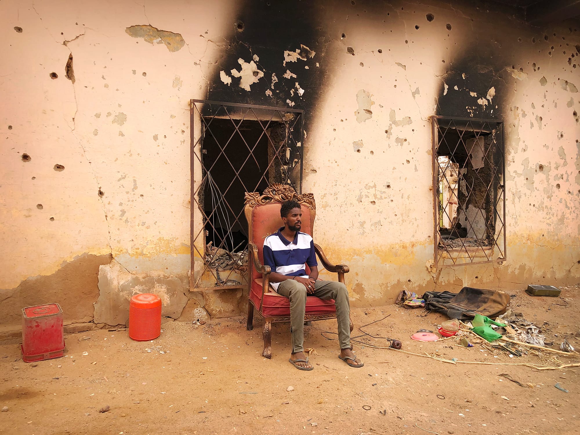 a man seated in a chair outside a fire-stained building