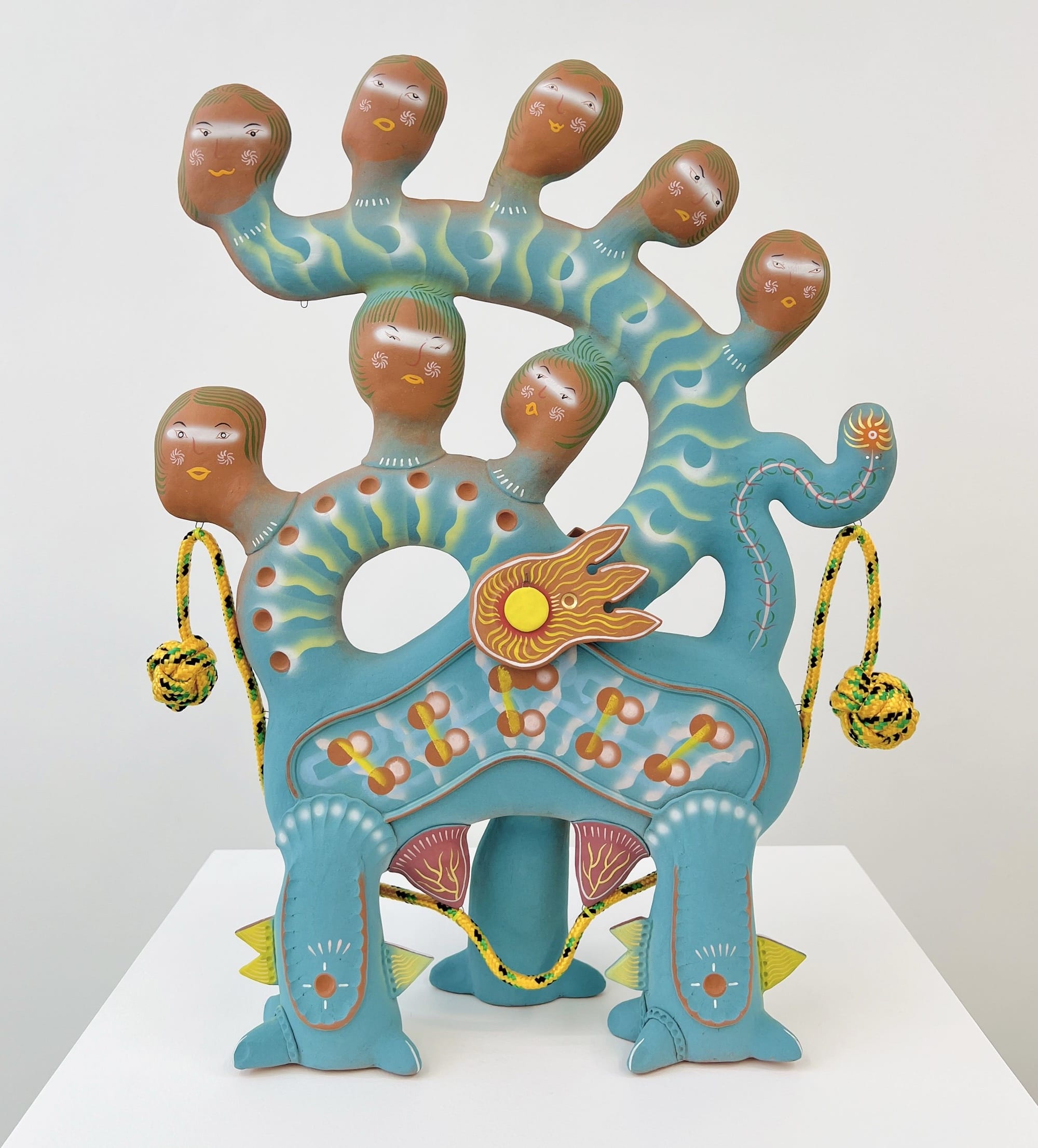 A ceramic sculpture by Chenlu Hu featuring an abstract, mythical character with numerous heads on a serpentine, teal body