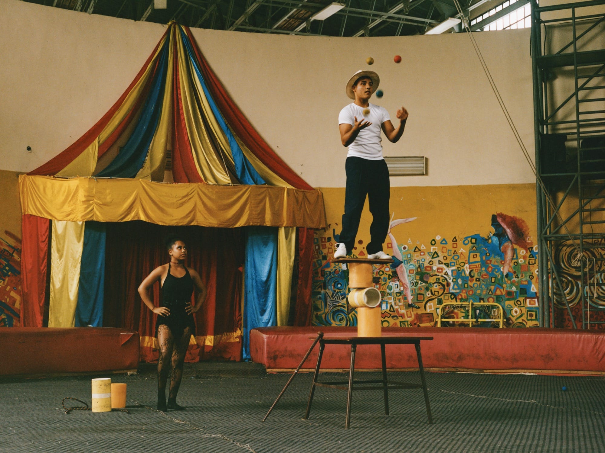 a photo by Constanze Han of circus performers, one juggling, in a primary colored Cuban hall