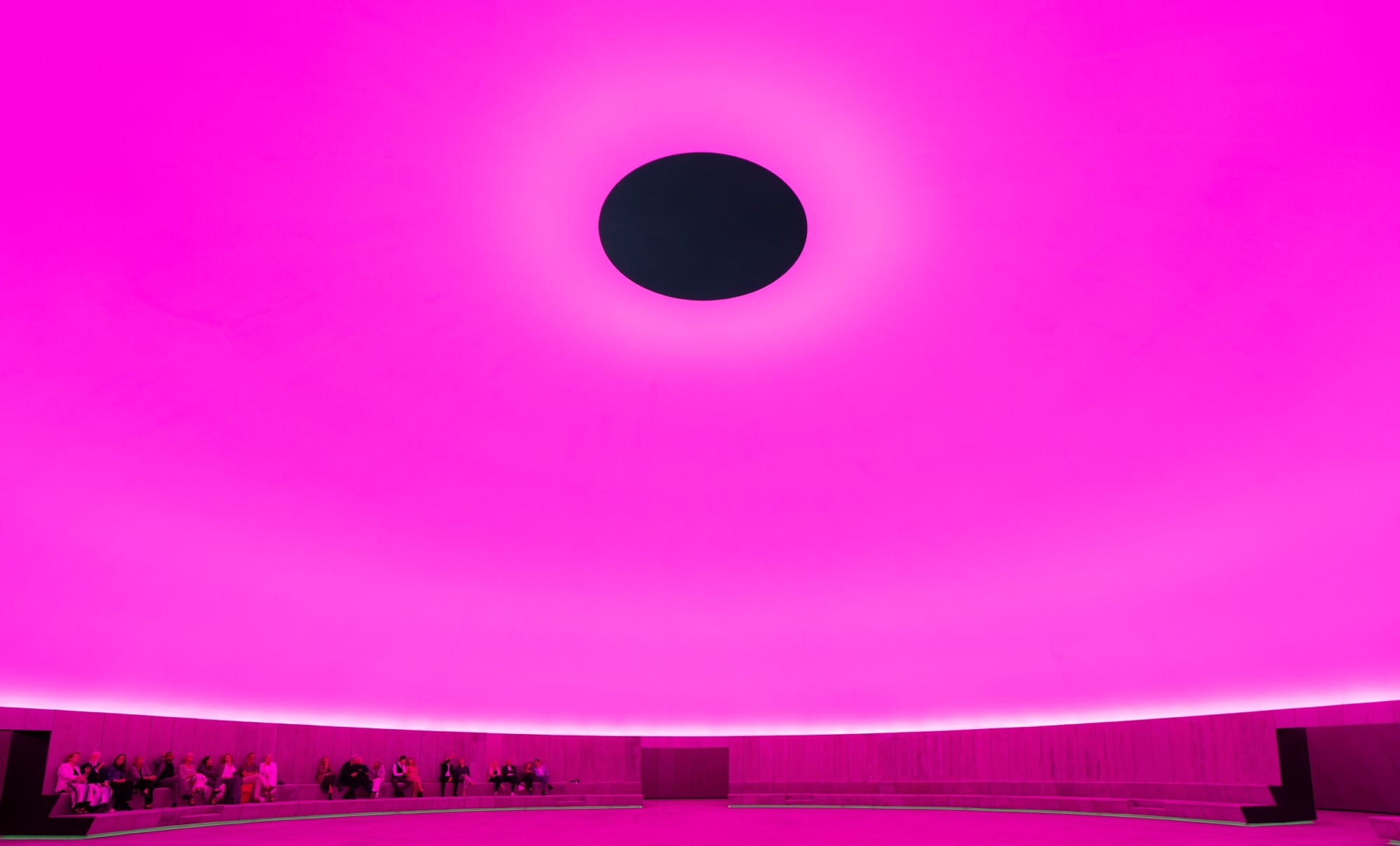 Visitors sit inside of James Turrell's Aarhus 'Skyspace' artwork at ARoS as it is illuminated bright pink