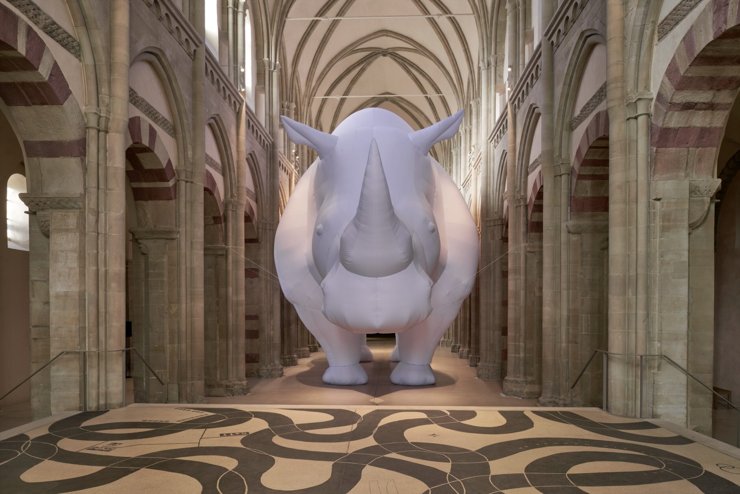A giant inflated sculpture by Itamar Gov of a gray rhinoceros amid Romanesque church architecture