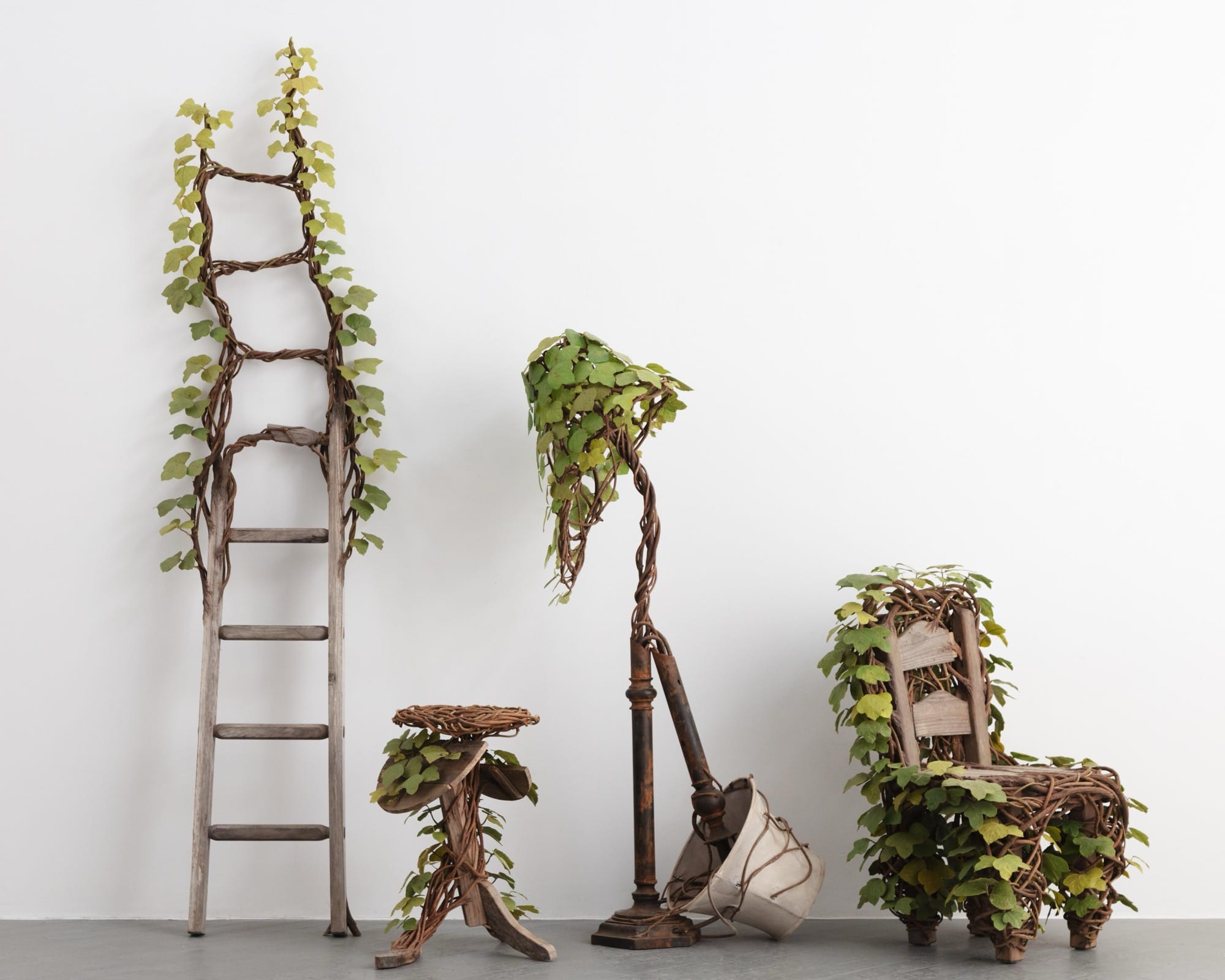 a collection of four wooden sculptures by Joyce Lin, including a ladder, table, floor lamp, and chair, all covered in green kudzu plants