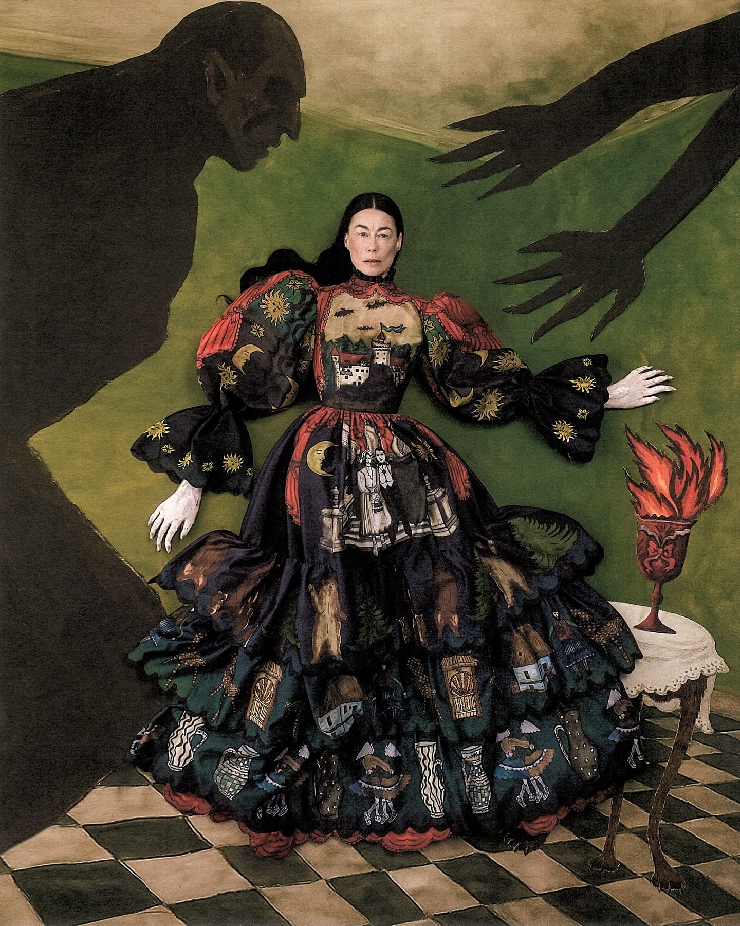 an editorial flat-lay portrait by Szilveszter Makó of a woman in an ornate gown. the background consists of a checkered floor and two dimensional silhouettes of a man and arms reaching for her