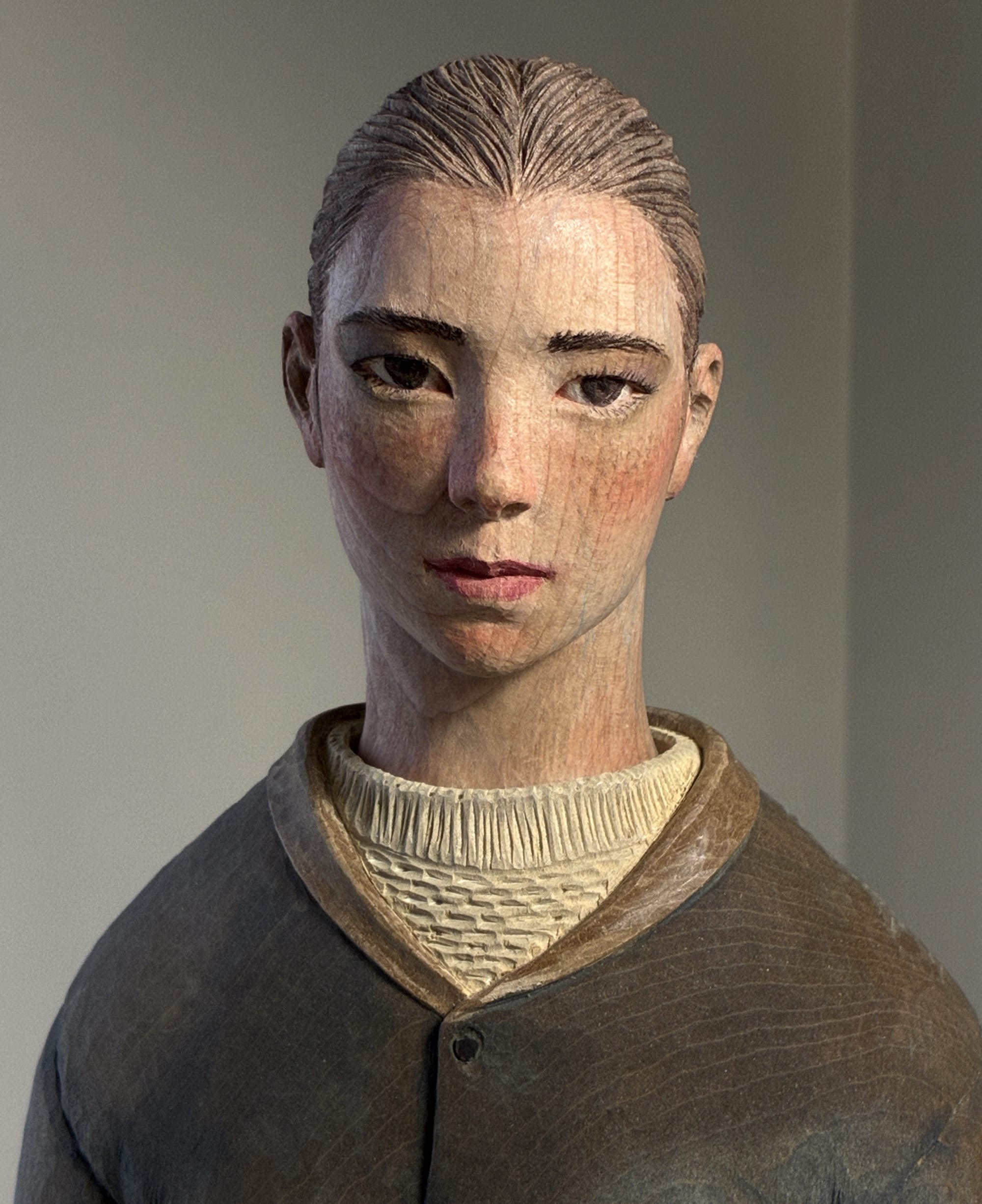 A detail of a figurative, painted wood sculpture of a young man by Shinsuke Inoue
