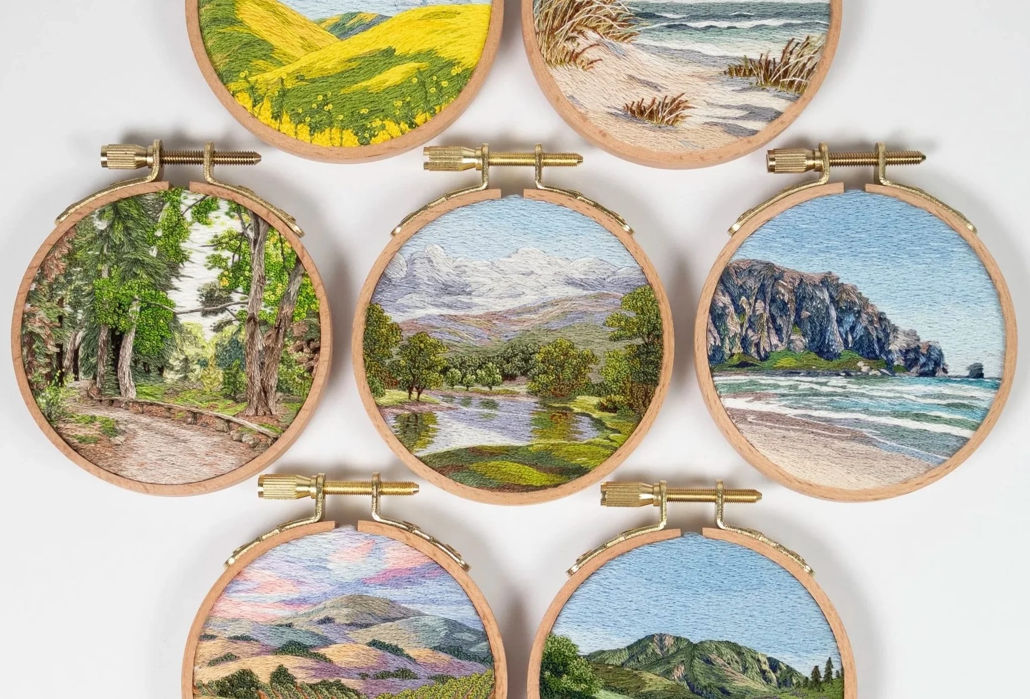 a collection of lush landscape embroideries in light wood hoops by Cassandra Dias