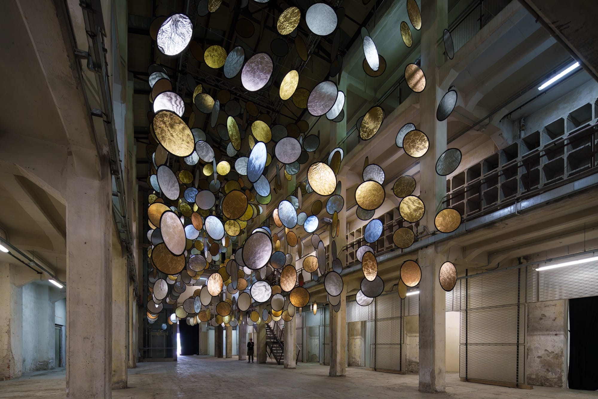 A large interior installation of metallic discs hanging from the ceiling in an industrial space