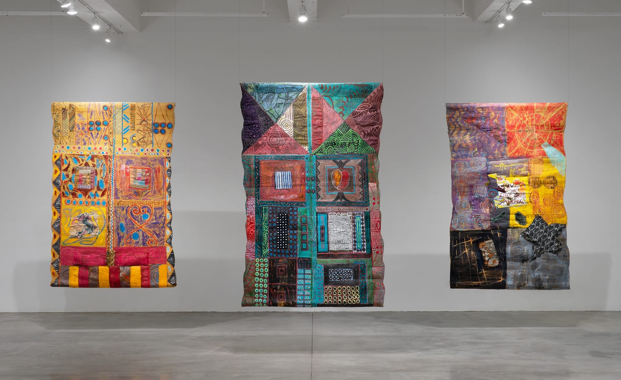 an installation image of three vibrantly painted and stitched abstract compositions by Pacita Abad