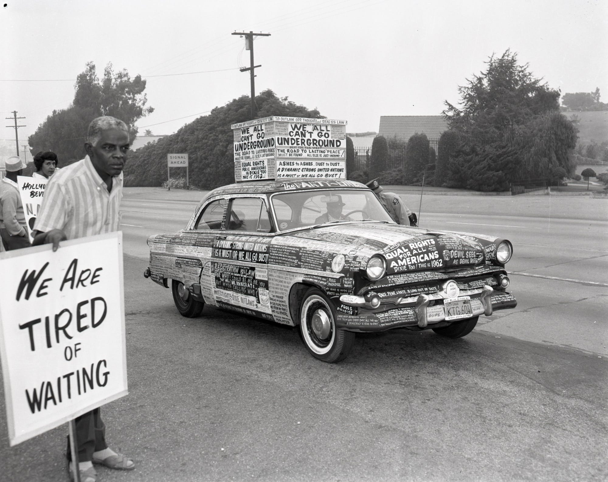 a black and white photo of a man and a car holding protest signs
