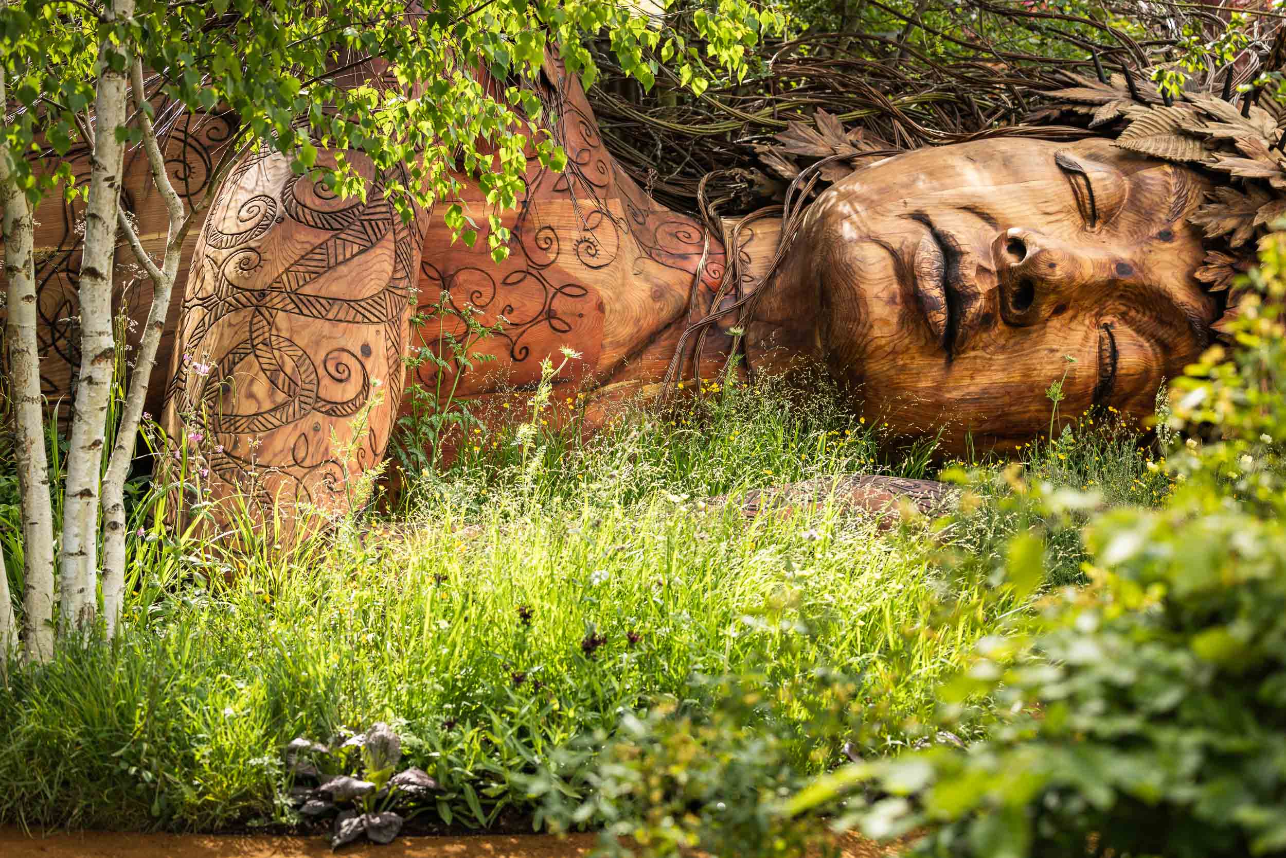 a wooden sculpture of Gaia amid a garden designed by Sarah Eberle at the RHS Chelsea Flower Show