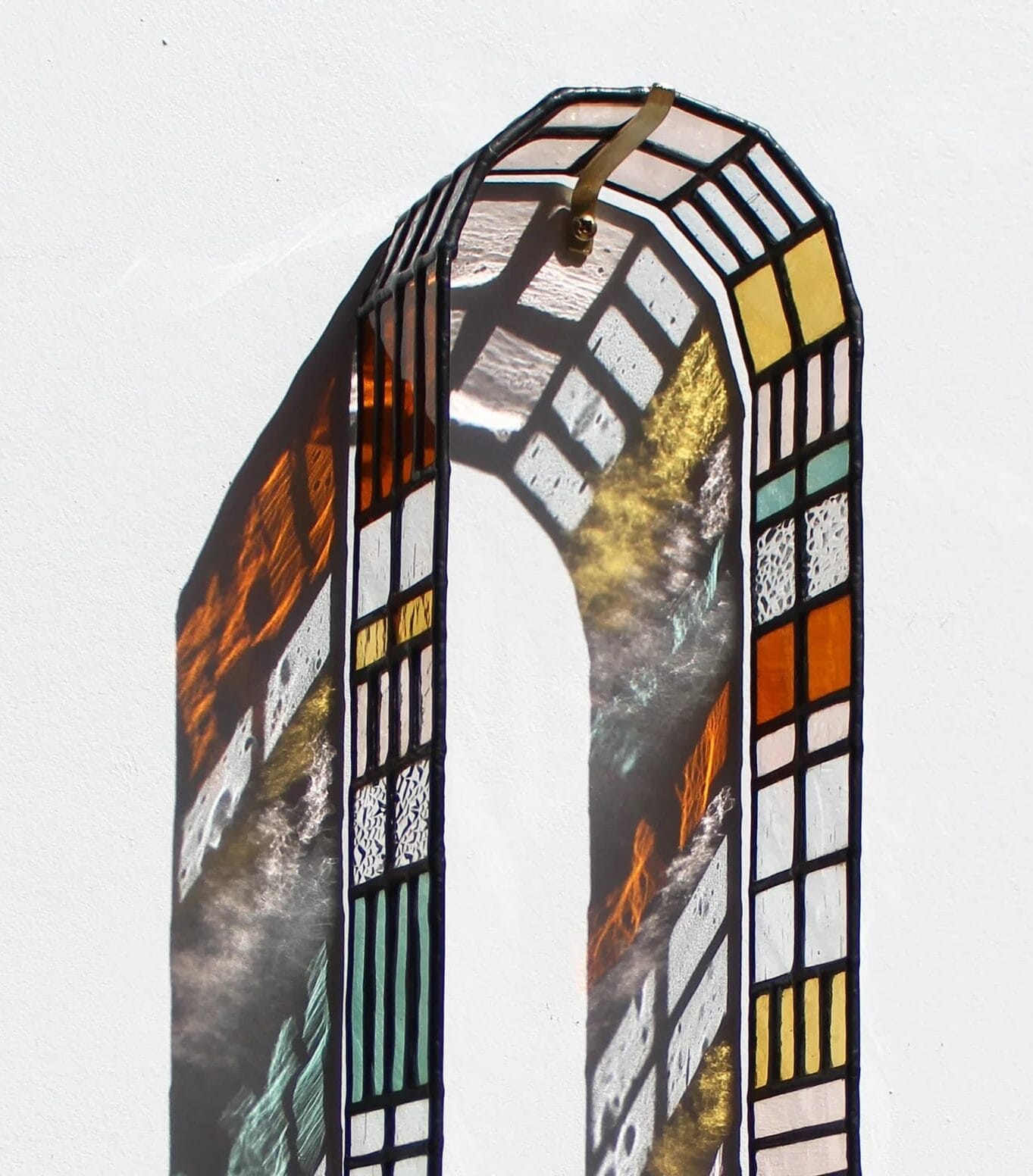 a sculptural arc of stained glass casting colorful patterns on a wall