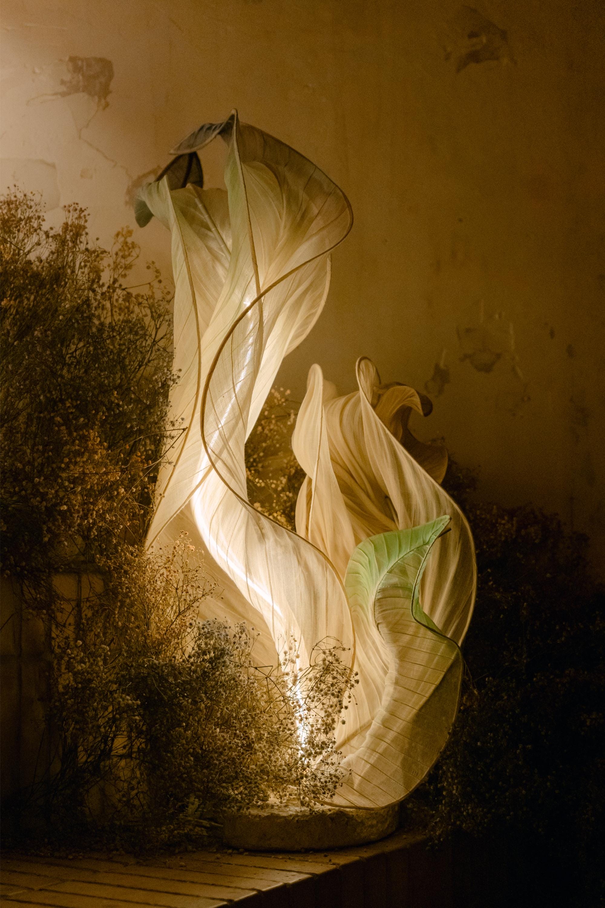 A dynamic sculptural lamp by Mirei Monticelli with light glowing through sheer textiles in hues of cream and light green