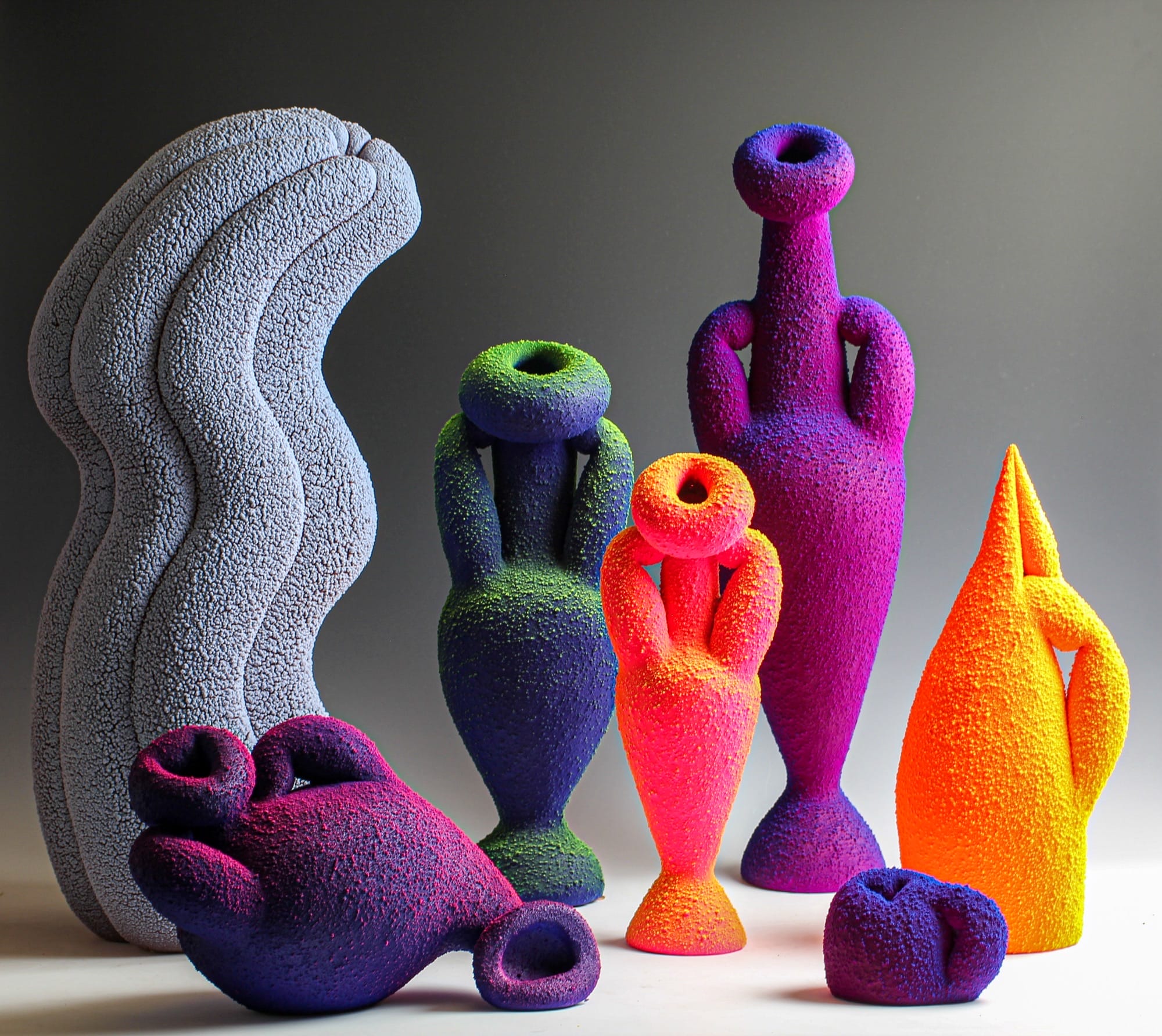 a group of seemingly glowing or fluorescing vase sculptures in different colors and pudgy shapes