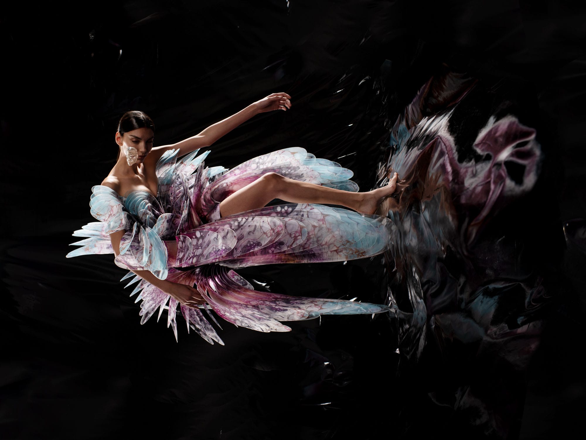 a model wears a sculptural, high-tech dress by Iris Van Herpen, photographed as if she's standing horizontally on a wall