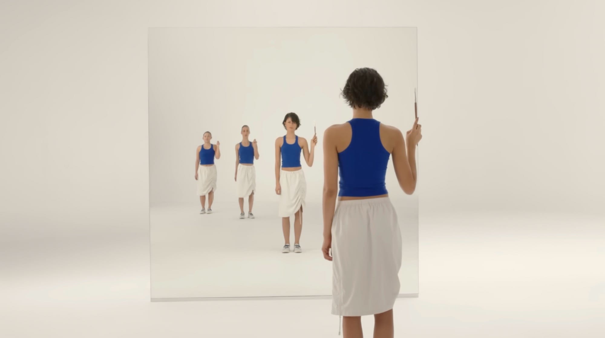 a still from an ad featuring Zendaya showing her wearing a blue and white outfit and looking into a mirror where she has three reflections