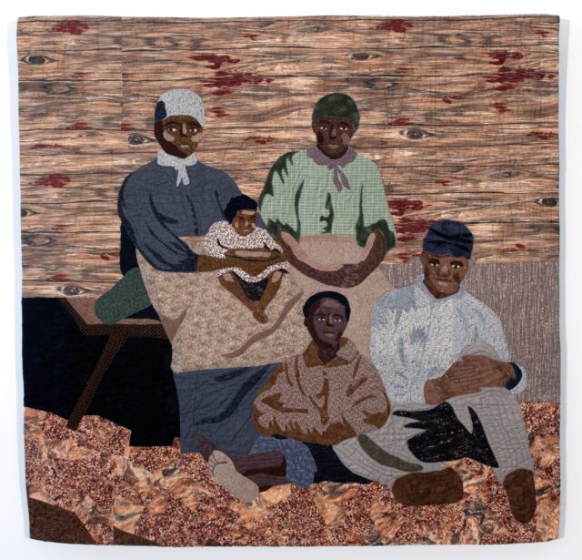 a graphic quilt featuring a Black family, possibly inspired by a historical photo, waiting for the Freedom Train